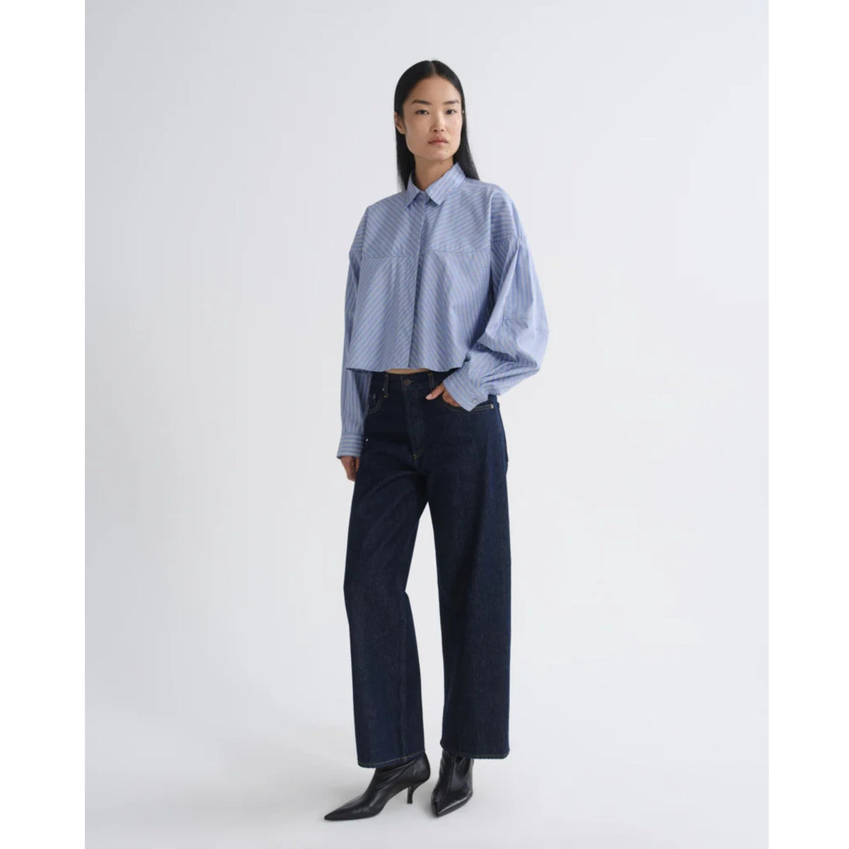 Full-length front view of a model wearing the blue and white striped AGOLDE Agnes Shirt tucked into dark navy pants against a light gray background.