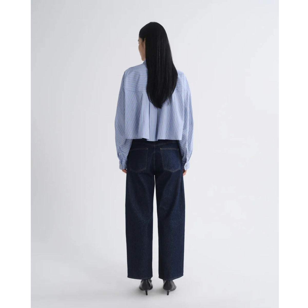 Full-length back view of a model wearing the AGOLDE Agnes Shirt in Meyer Stripe Blue/White paired with dark navy pants against a light gray background.