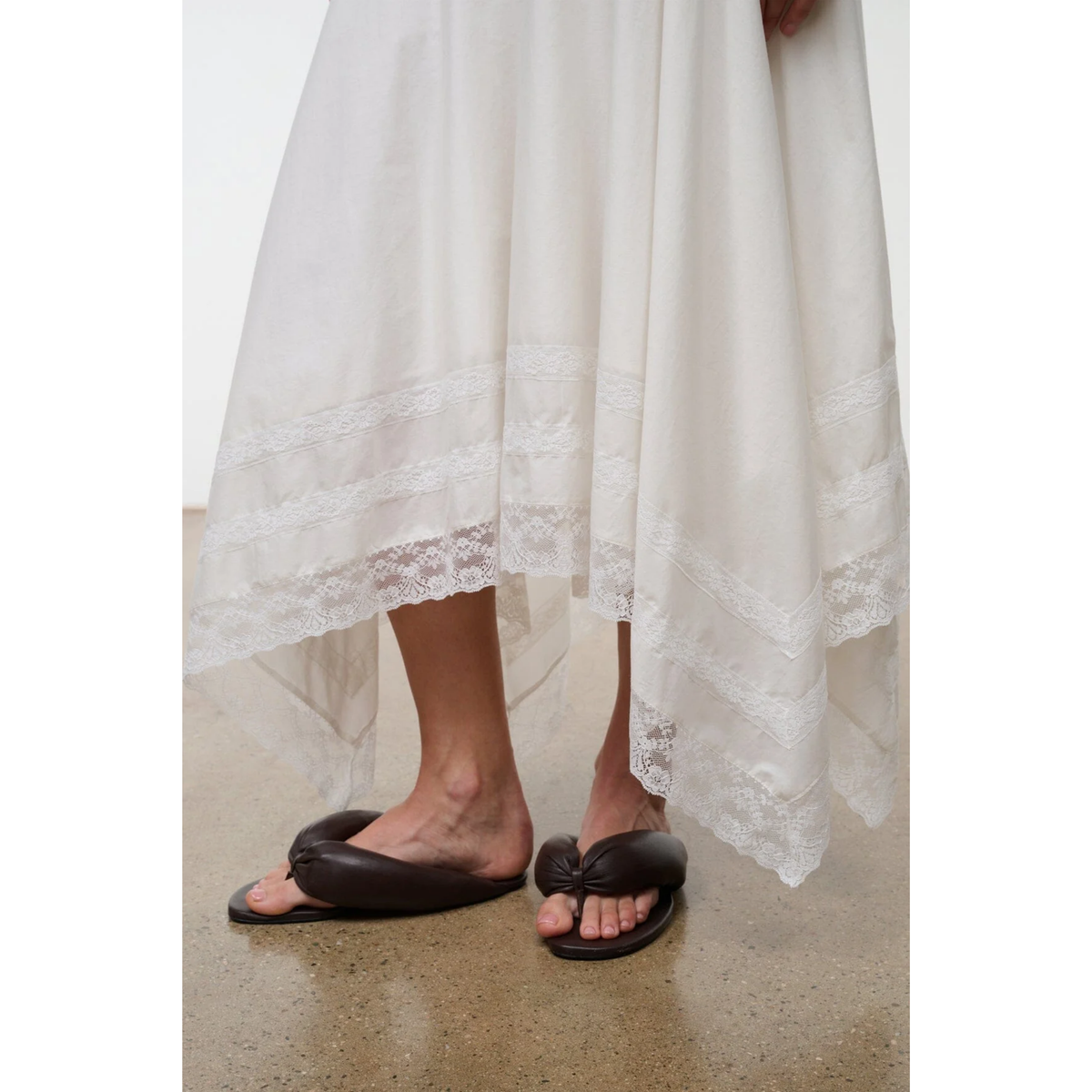 White lace dress with brown sandals on a neutral background