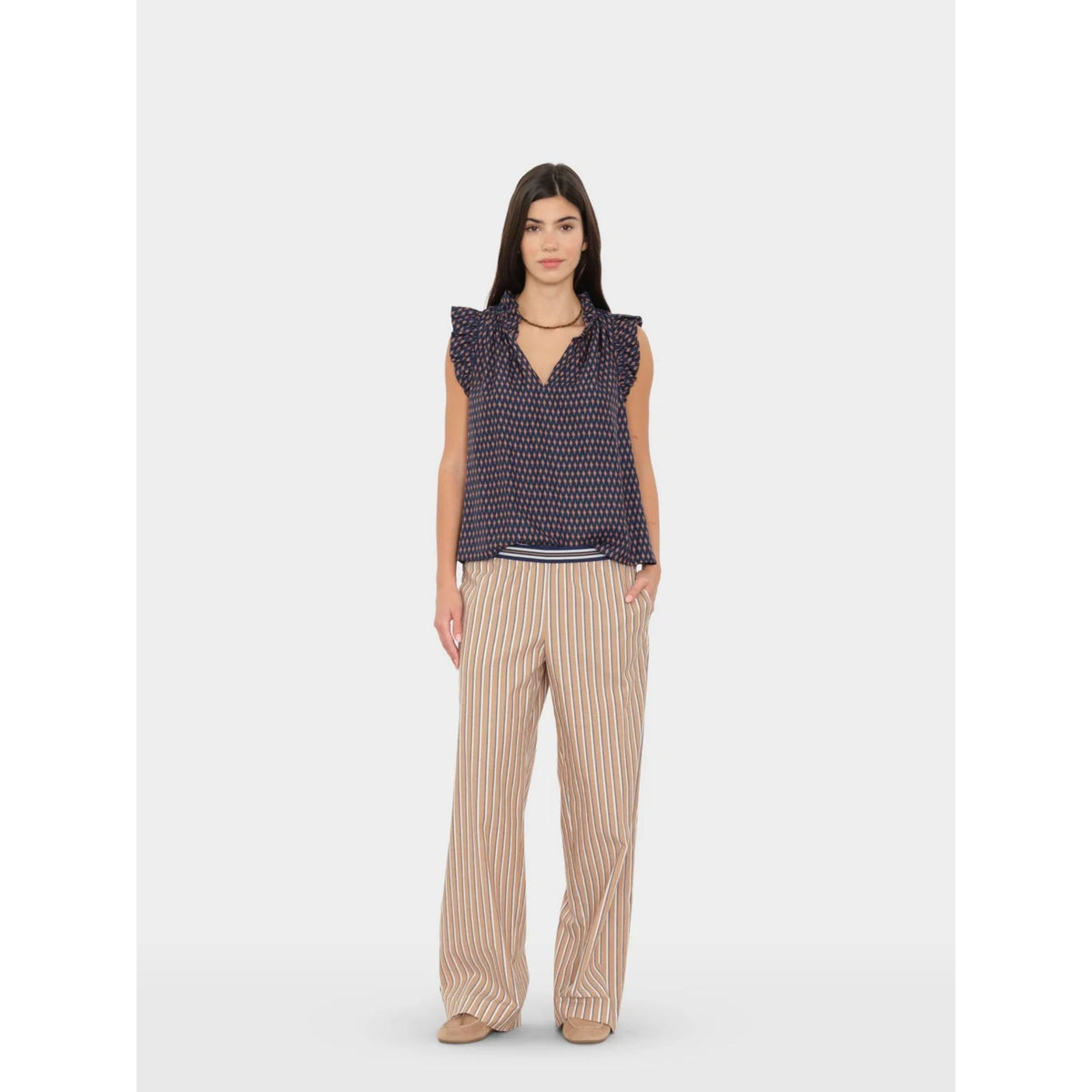 Full-length front view of a model wearing the tan striped Alto Pant styled with a dark sleeveless top.