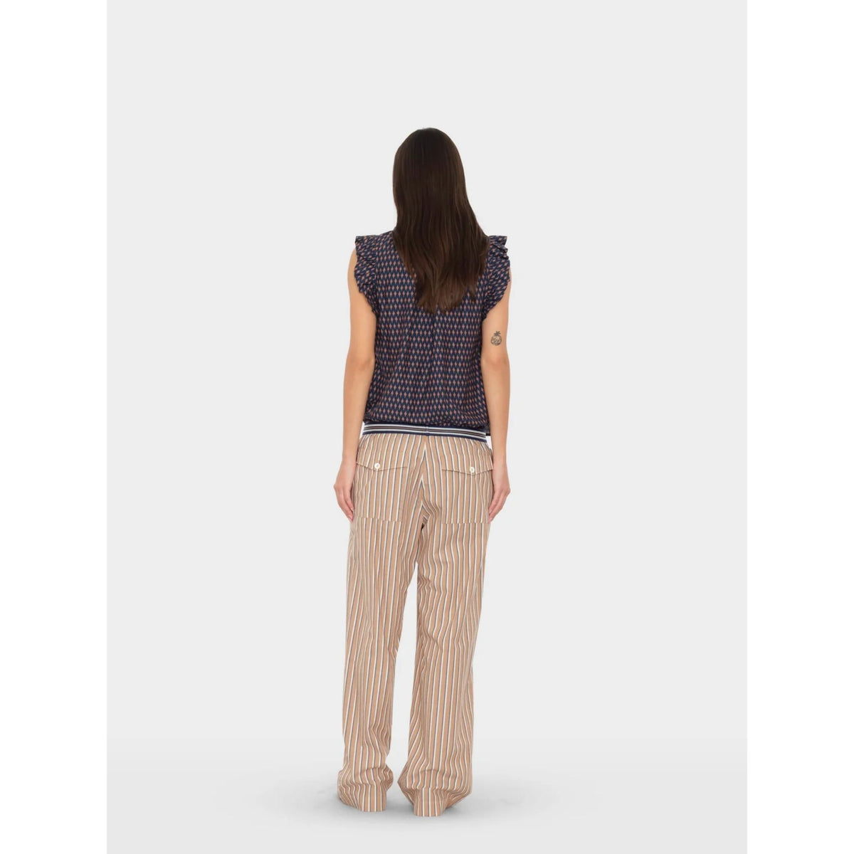 Full-length back view of a model wearing the tan striped Alto Pant styled with a dark sleeveless top.