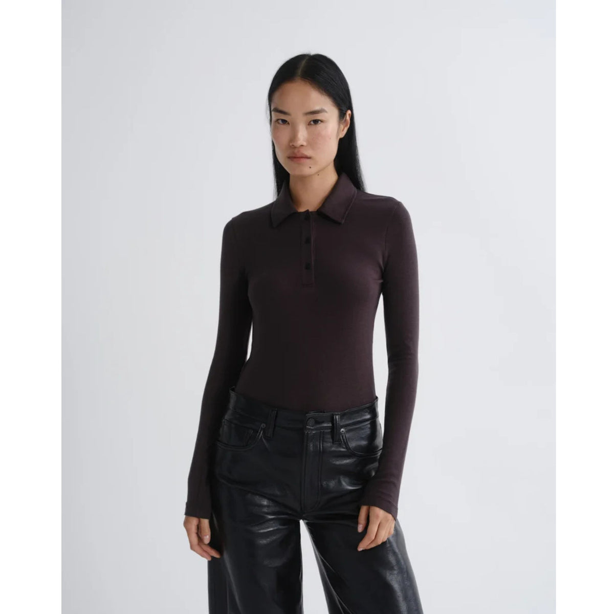 Model wearing AGOLDE Amos Polo in Forge brown long-sleeve ribbed shirt paired with dark leather pants against a light gray background.