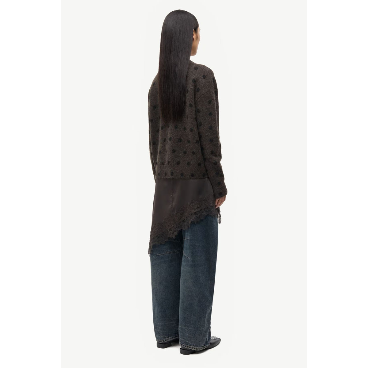 A model shown from the back wearing a dark brown textured knit cardigan with a scalloped lace hem, paired with wide-leg blue jeans, against a plain off-white background.