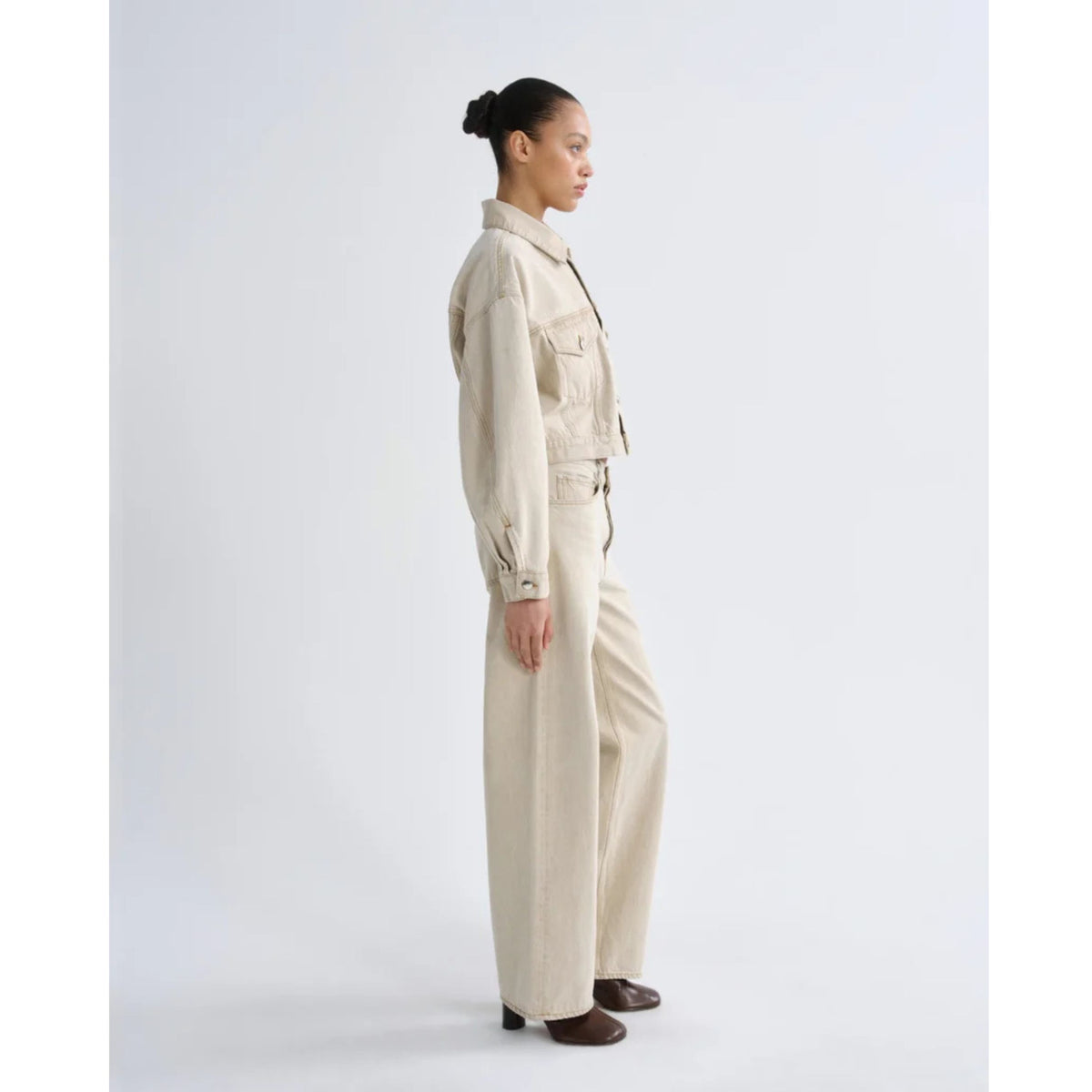 Side profile view of a model wearing a light sand cropped jacket and AGOLDE Arc Jeans in Arena against a light gray background.