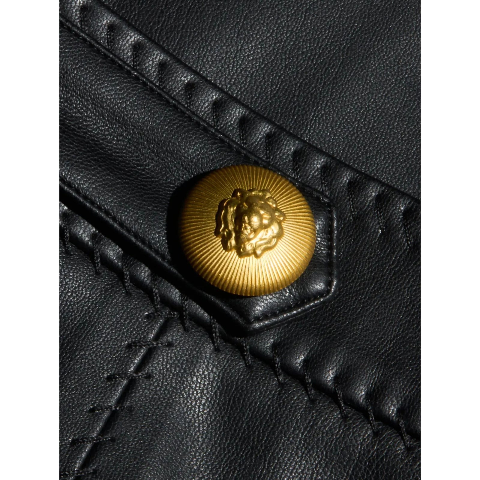 A black faux-leather mini skirt with vertical seam panels and two gold-tone metal buttons at the waistband, shown against a solid beige background.