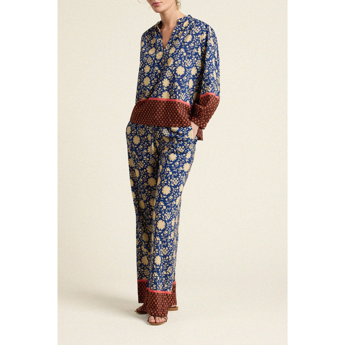 A model wearing a two-piece pajama set with a blue and beige floral print, featuring a matching long-sleeve top and pants with contrasting brown patterned cuffs and hem.