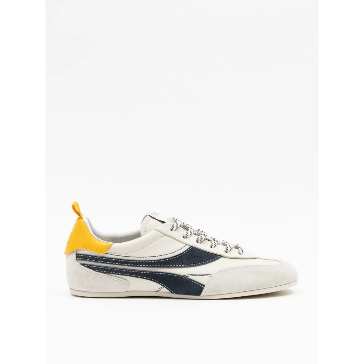 A low-top sneaker in off-white suede and navy blue leather, featuring a bright yellow heel tab and matching yellow pull loop, with white laces.