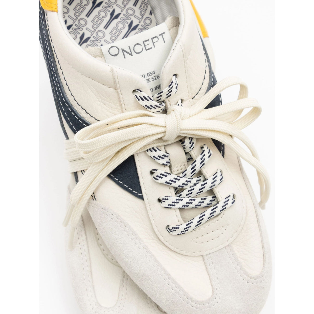 A close-up of a Oncept brand sneaker featuring off-white leather panels, navy blue side accents, and cream-colored laces tied in a bow. The Oncept logo is visible on the inner collar label.