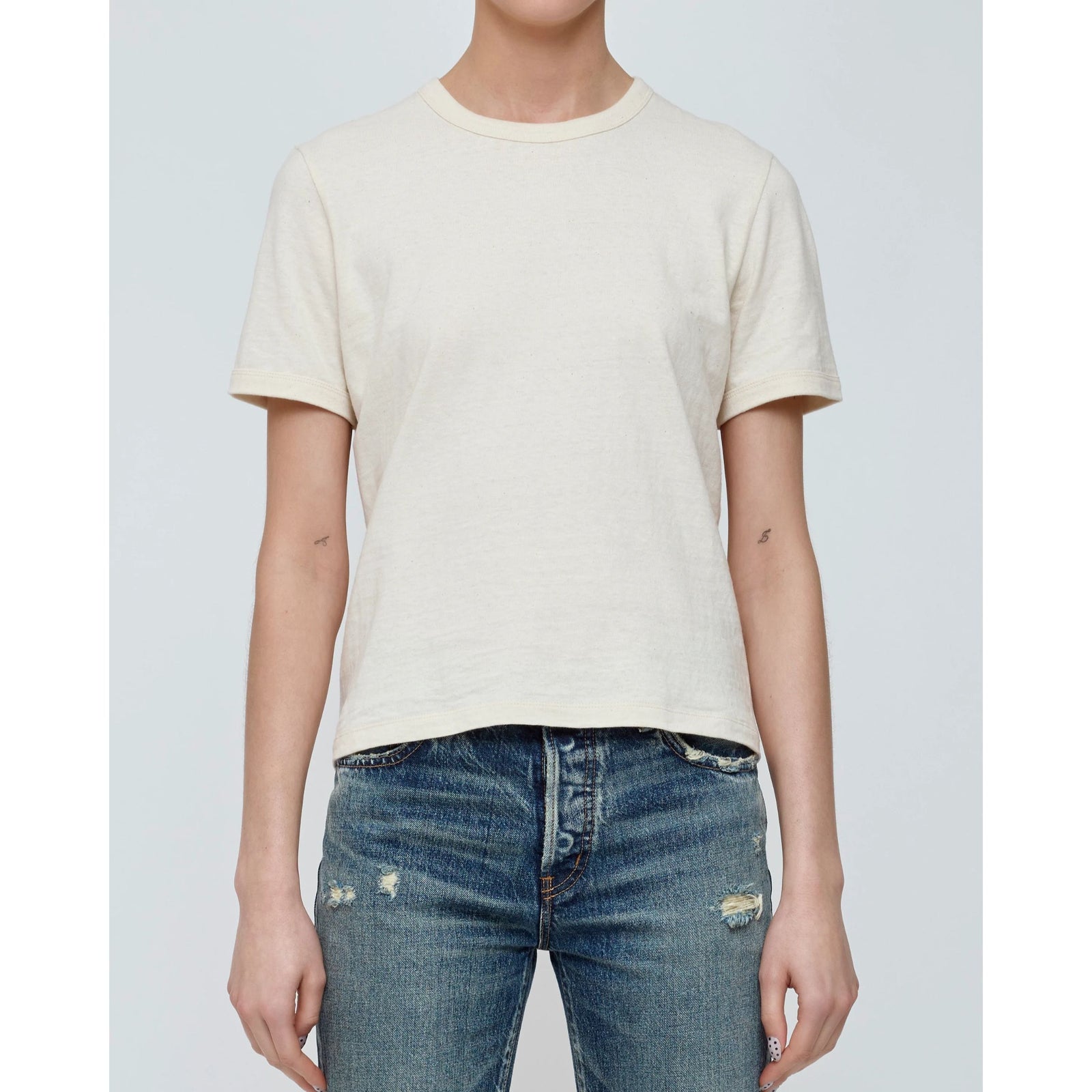 Front flat lay view of the short-sleeve "Basic Tee" in off-white crewneck cotton jersey against a light neutral background.