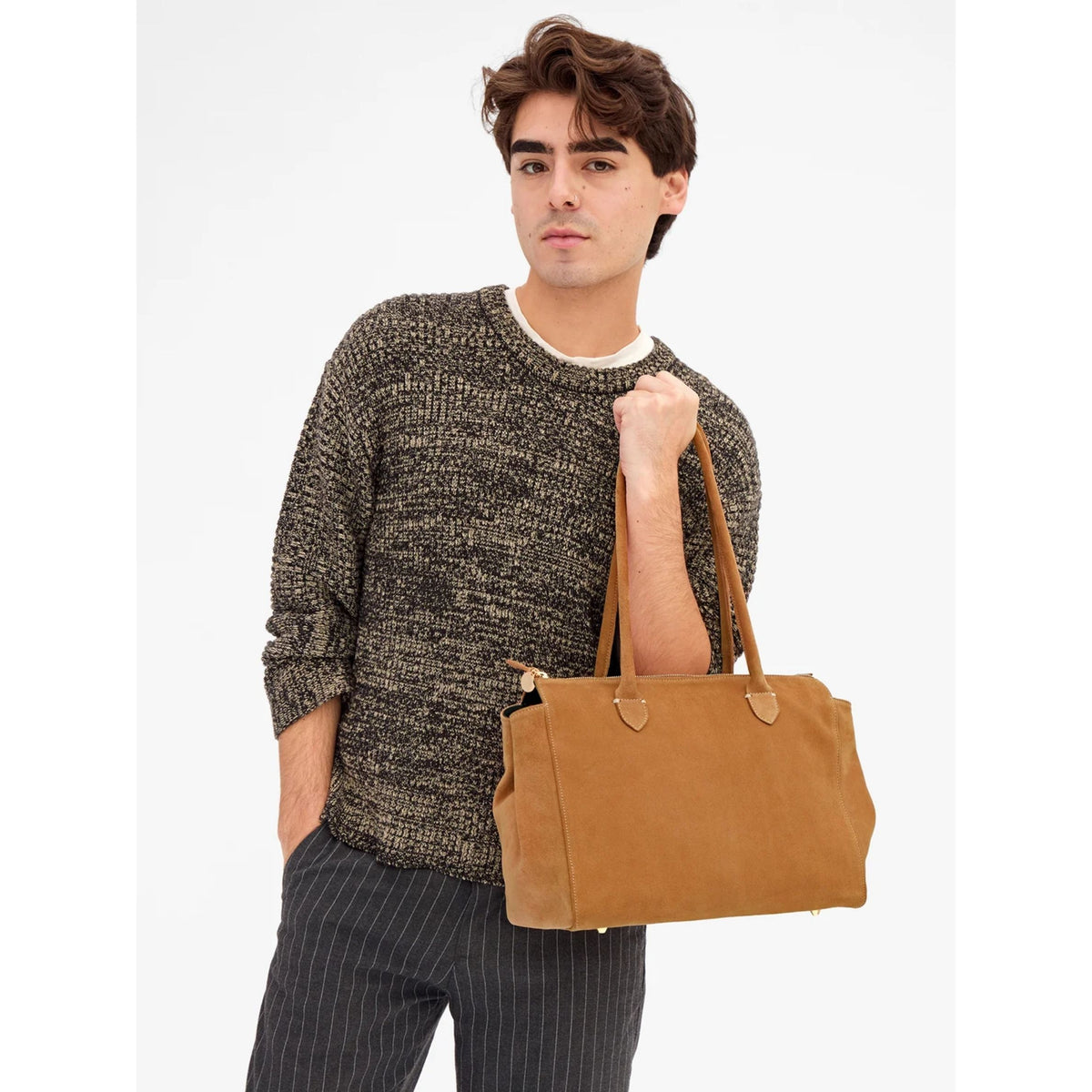 Front waist-up shot of a model wearing a grey patterned sweater, carrying the Caramel brown suede Beatrice tote bag by its shoulder strap.