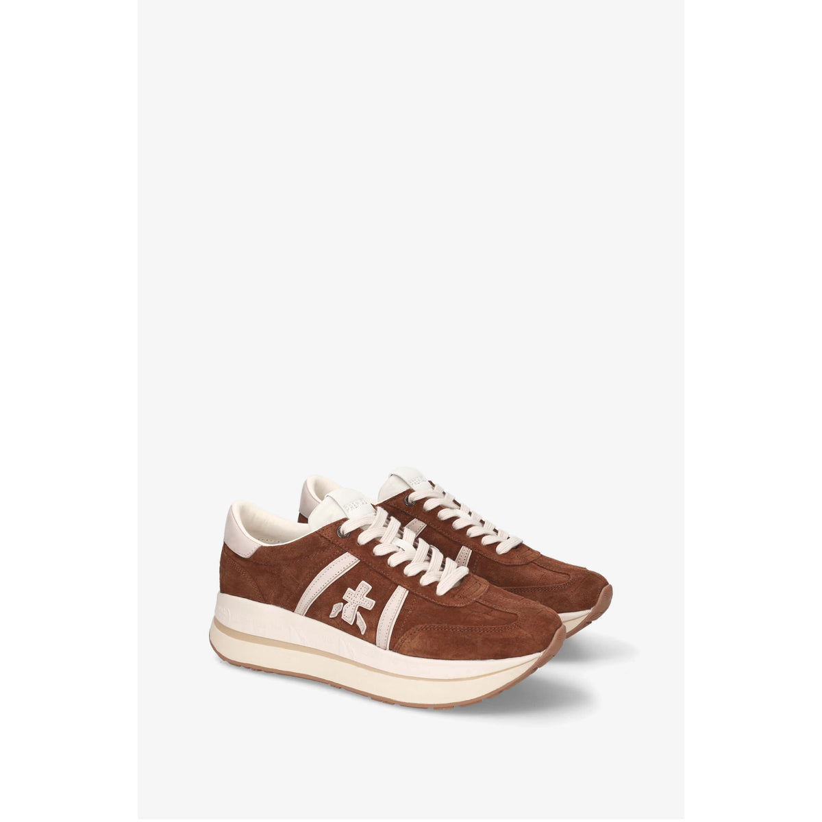 A pair of low-top sneakers in brown suede and cream leather, featuring a cream midsole and a white embroidered cross logo on the side, displayed against a light gray background.