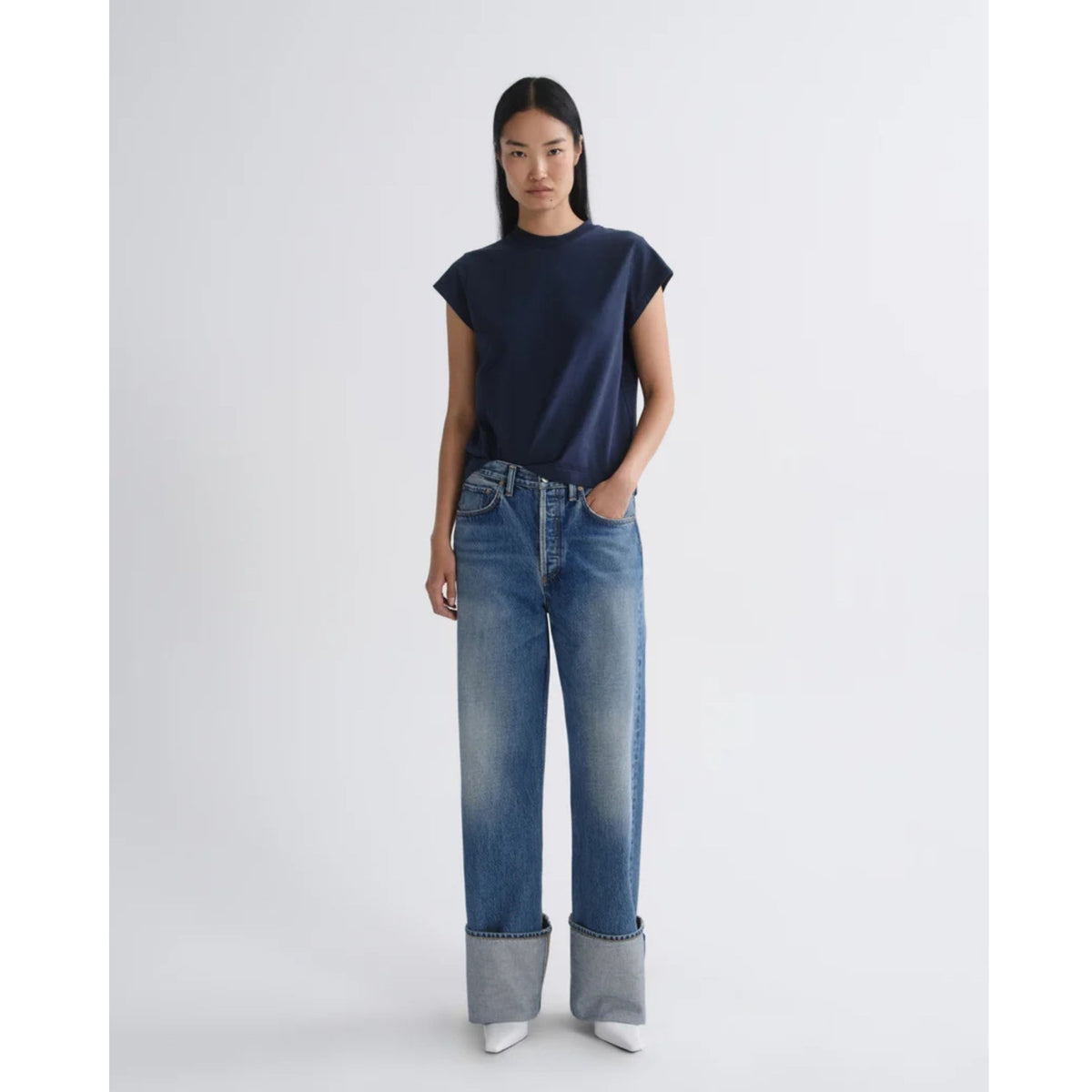 Full-length front view of a model wearing a short-sleeve dark navy top and AGOLDE Big Cuff Jeans in Liberty with wide folded cuffs against a light gray background.