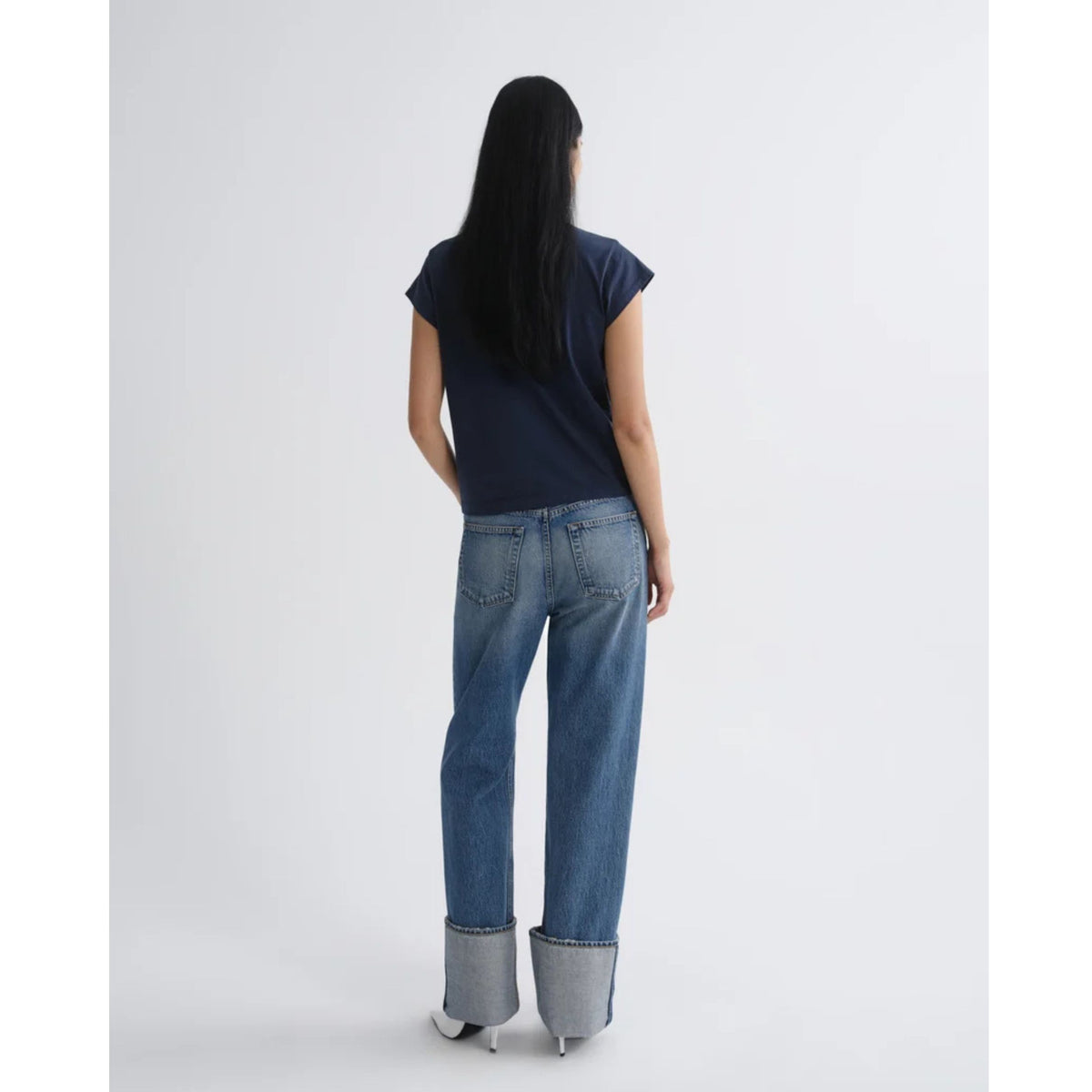 Back view of a model wearing a short-sleeve dark navy top and AGOLDE Big Cuff Jeans in Liberty against a light gray background.