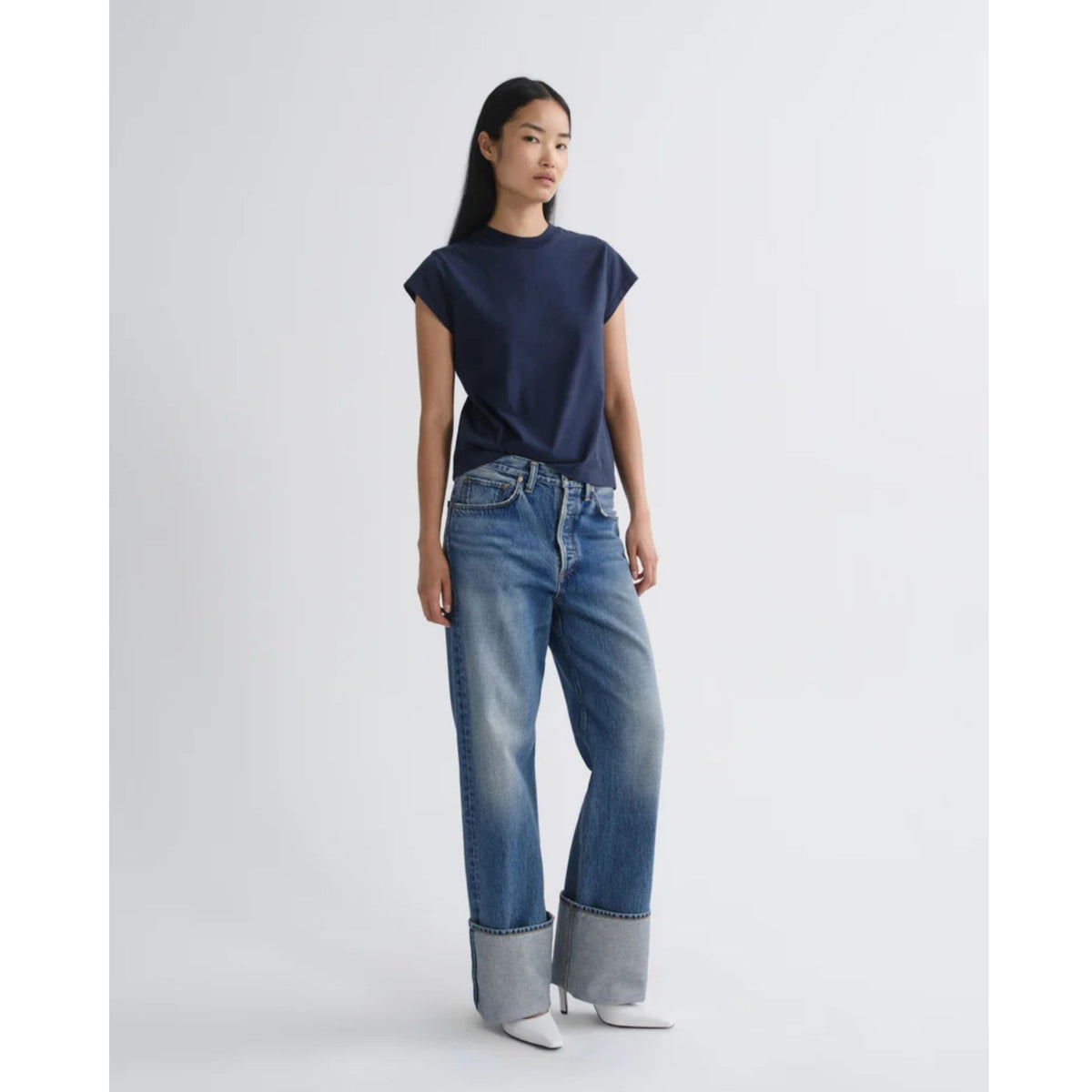 Three-quarters front view of a model wearing a dark navy short-sleeve top paired with cuffed AGOLDE Big Cuff Jeans in Liberty against a light gray background.