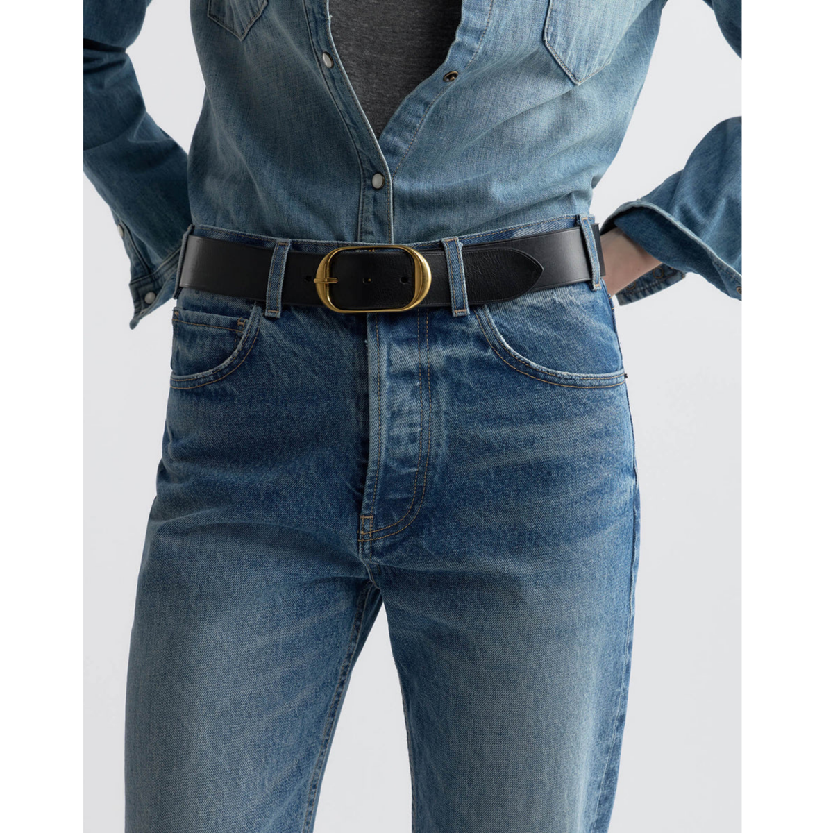 Person wearing a blue denim jumpsuit with a black belt on a white background