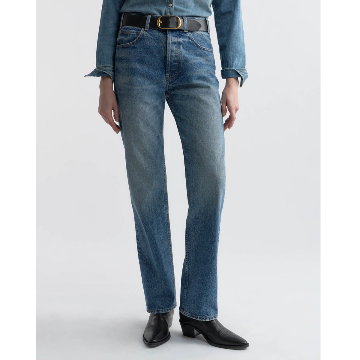 Person wearing blue jeans and black boots on a white background