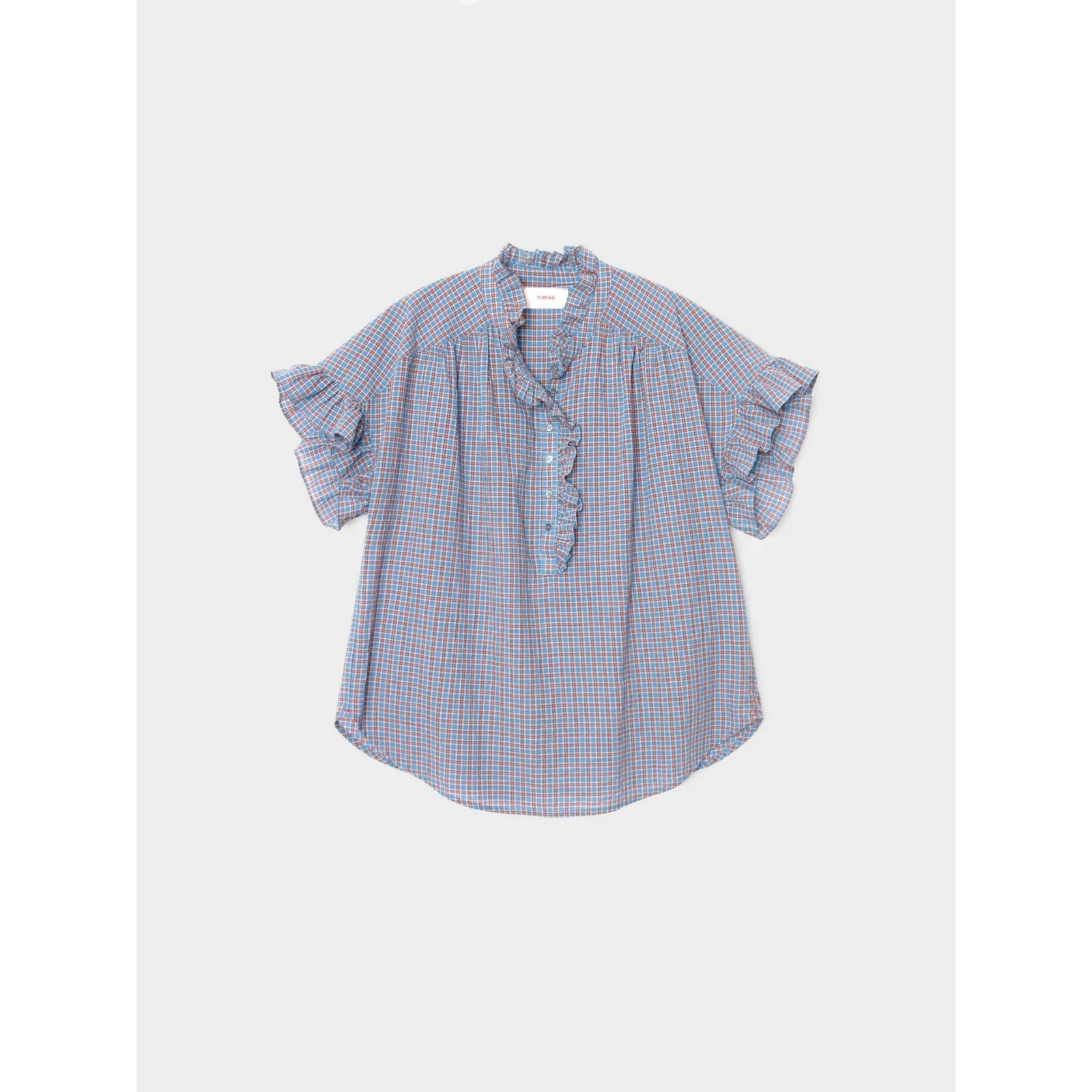 A short-sleeve blouse with a blue, red, and white gingham check pattern, featuring ruffled details on the collar and sleeve cuffs, laid flat against a light gray background.