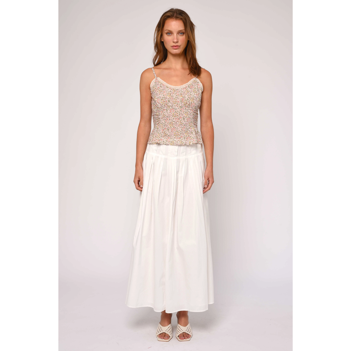 Woman wearing a sleeveless top and white skirt on a plain background