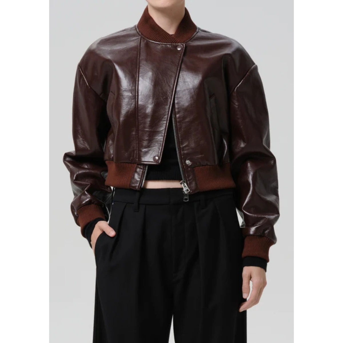 A cropped dark brown faux-leather bomber jacket with ribbed brown collar, cuffs, and hem, worn by a model with black trousers against a light gray background.