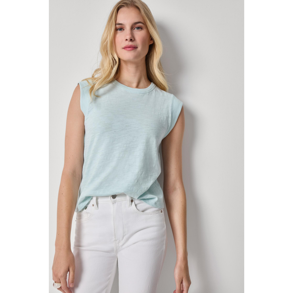 Woman wearing a light blue sleeveless top and white pants against a plain background