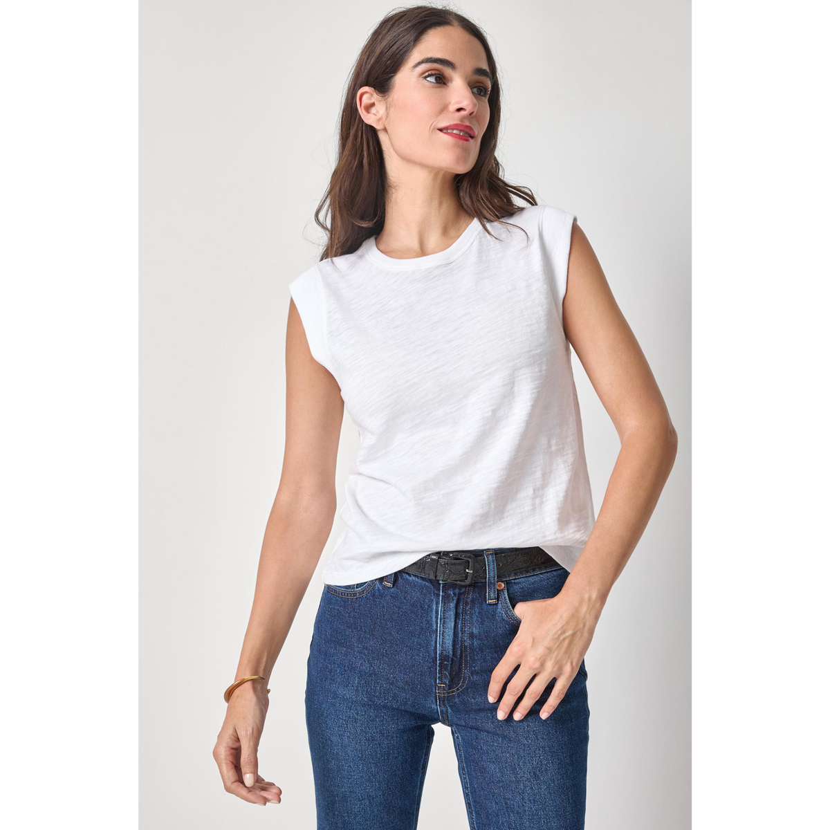 Woman wearing a white sleeveless top and blue jeans on a plain background