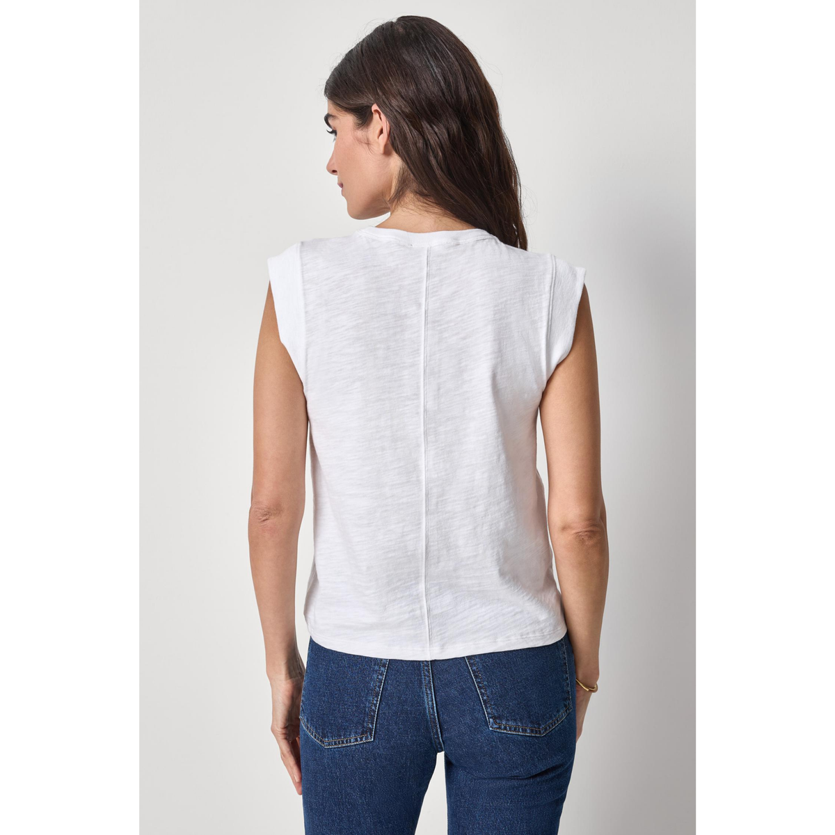 Woman wearing a white sleeveless top and blue jeans on a plain background
