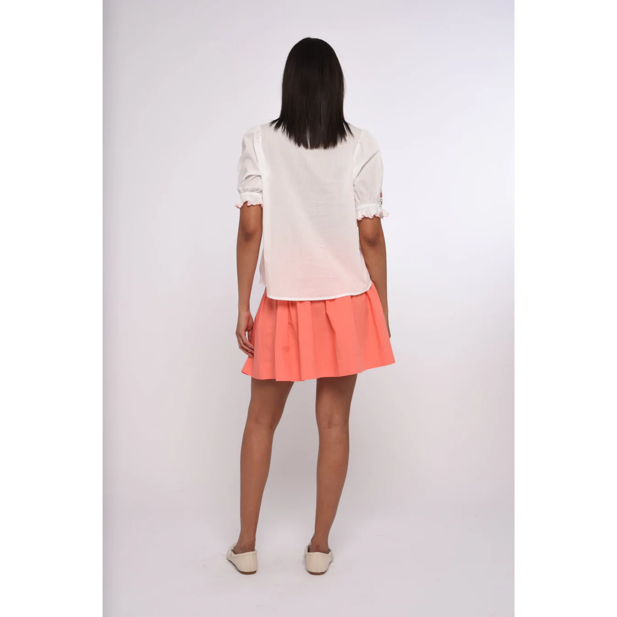 Woman wearing a white blouse and coral skirt on a plain background