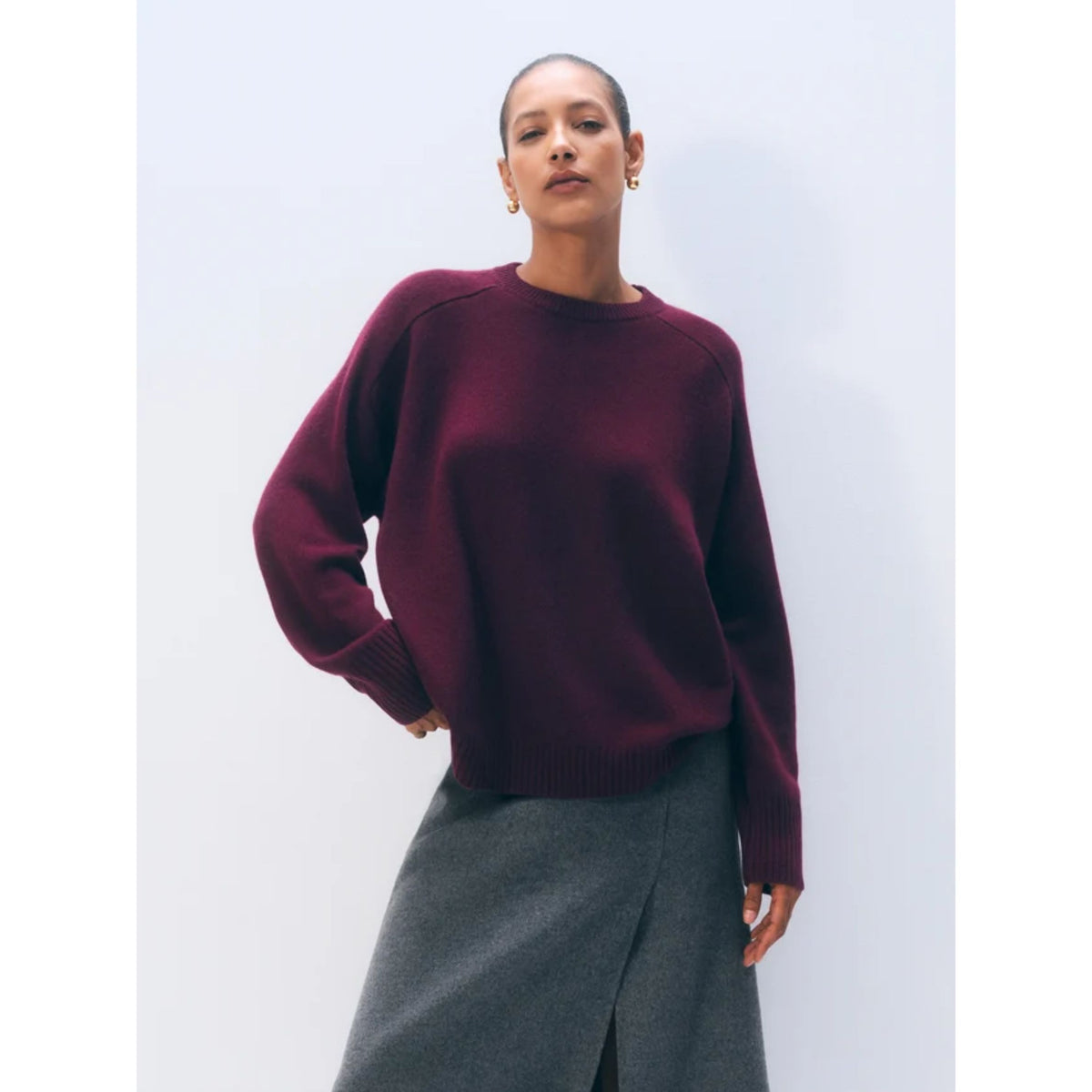 Front waist-up view of a model wearing the dark Sangria burgundy long-sleeve cashmere crewneck sweater, styled with a grey skirt.