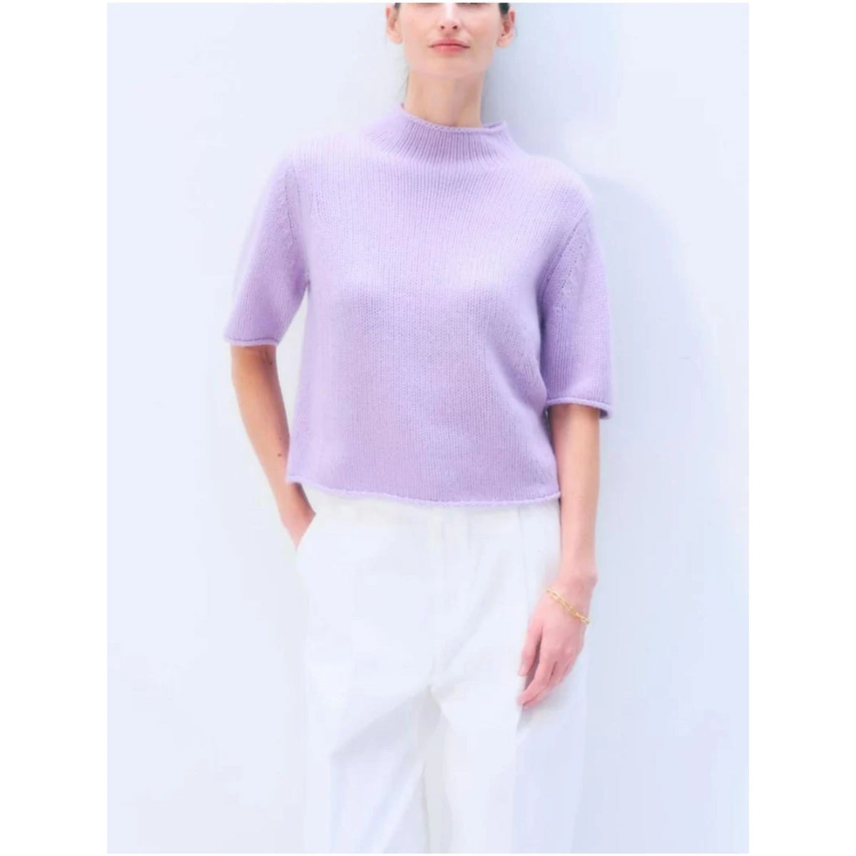 Front waist-up view of a model wearing the short-sleeve mock-neck cashmere tee in light lavender purple paired with white pants.