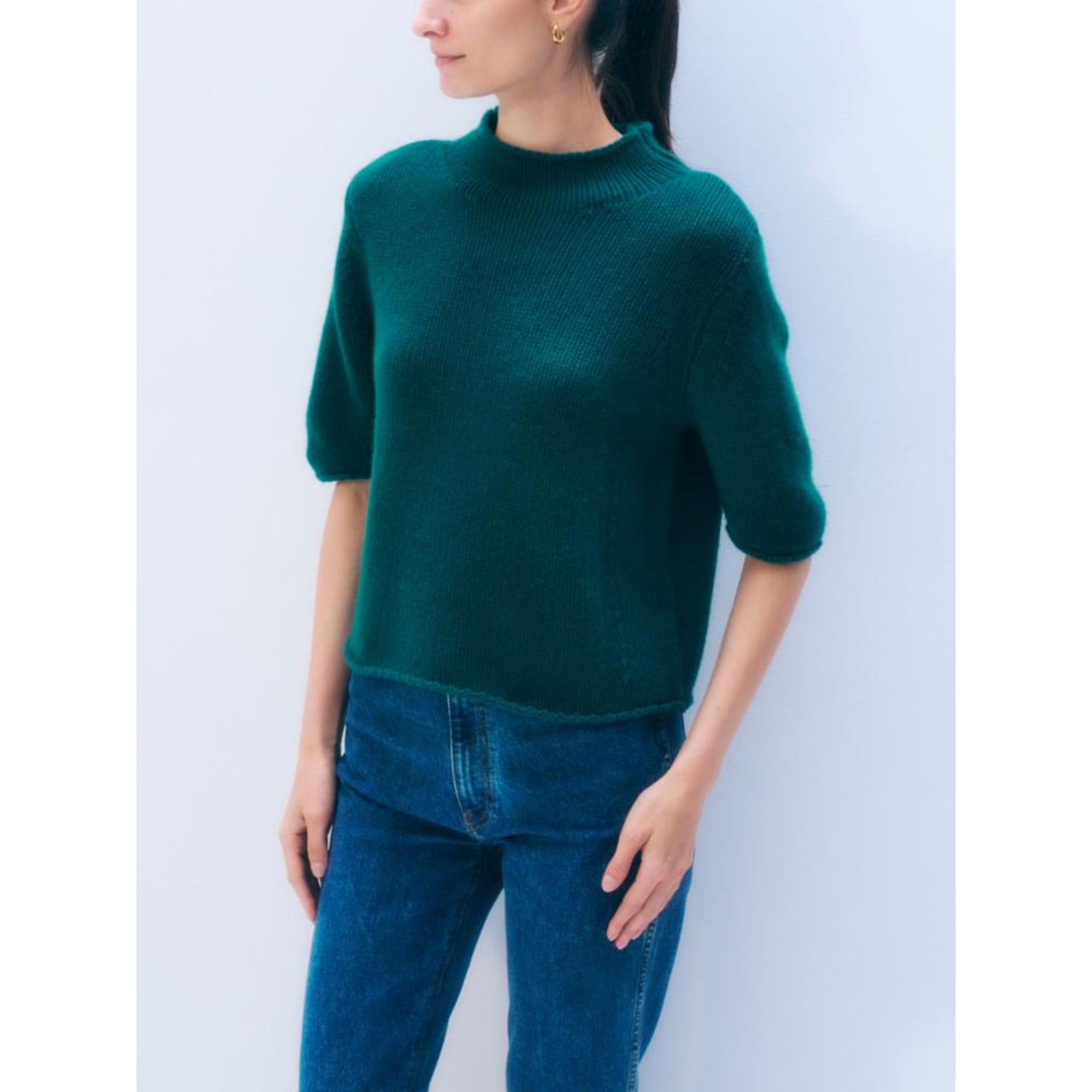 Half-body shot of a model wearing a short-sleeve dark teal green mock-neck cashmere tee, another model wearing the cashmere tee in lavender and then a flatlay of the cashmere tee in burgundy.