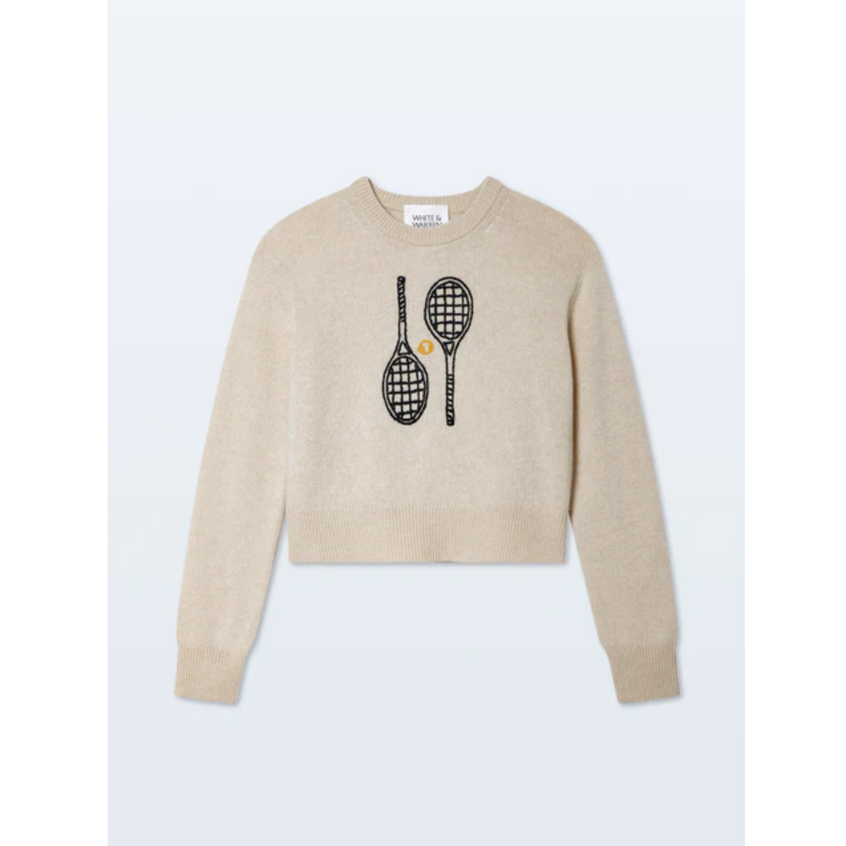 A cropped long-sleeve knit sweater in a light oatmeal beige color, featuring a graphic of two black tennis rackets with a small yellow tennis ball on the chest, displayed against a light gray background.