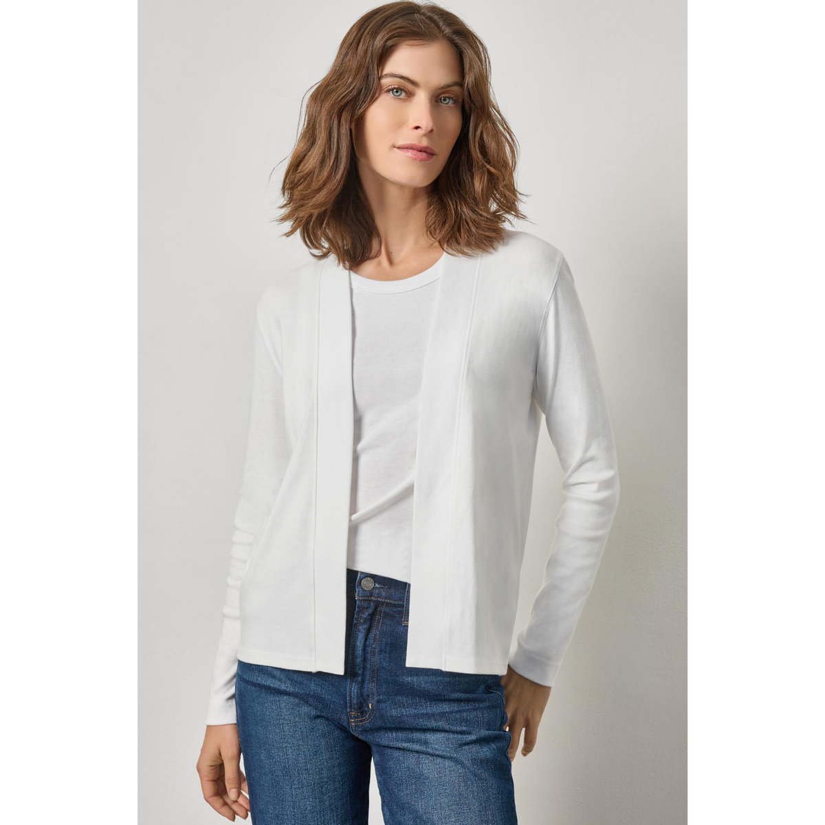 Woman wearing a white blouse and blue jeans against a plain background