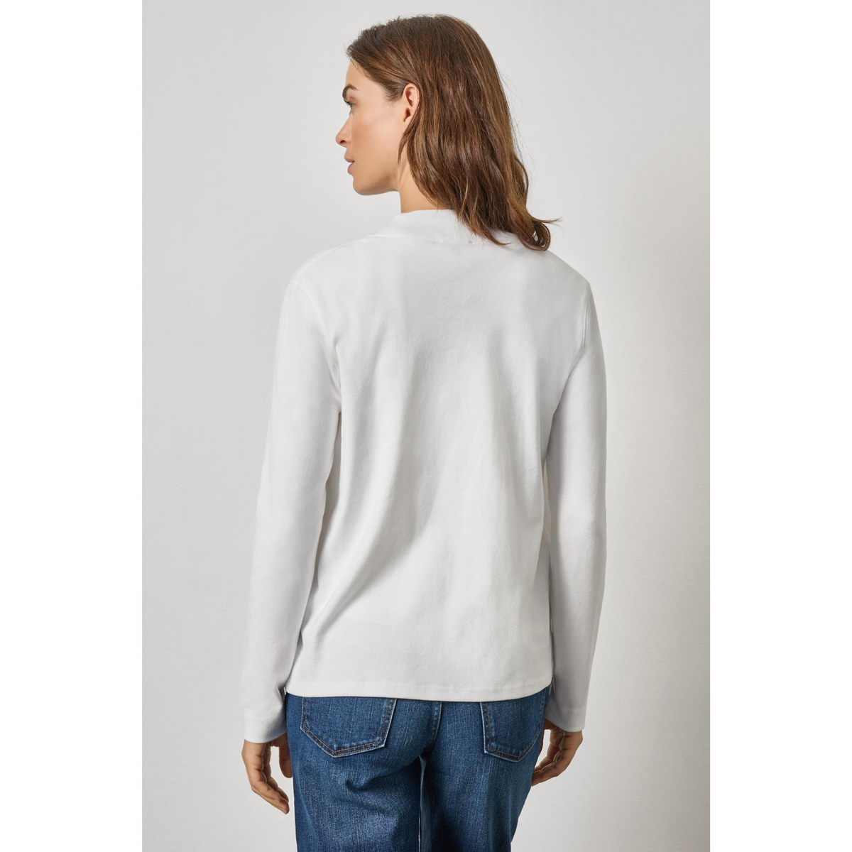 Woman wearing a light gray sweater and blue jeans against a plain background