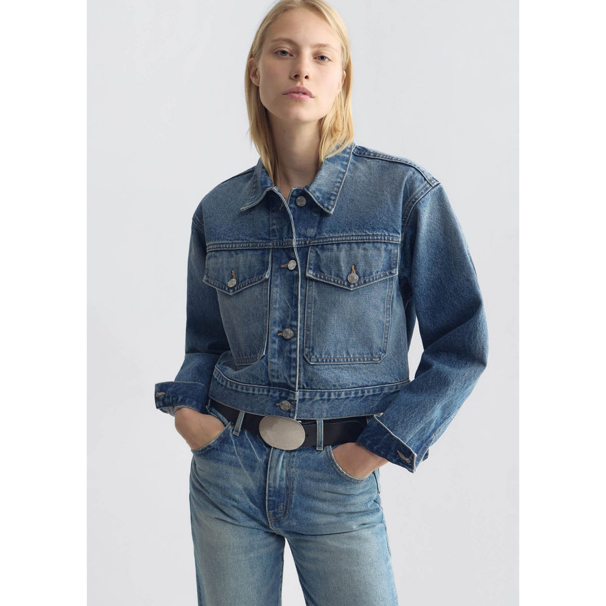 Medium shot of a model wearing the cropped blue denim jacket over a dark top.