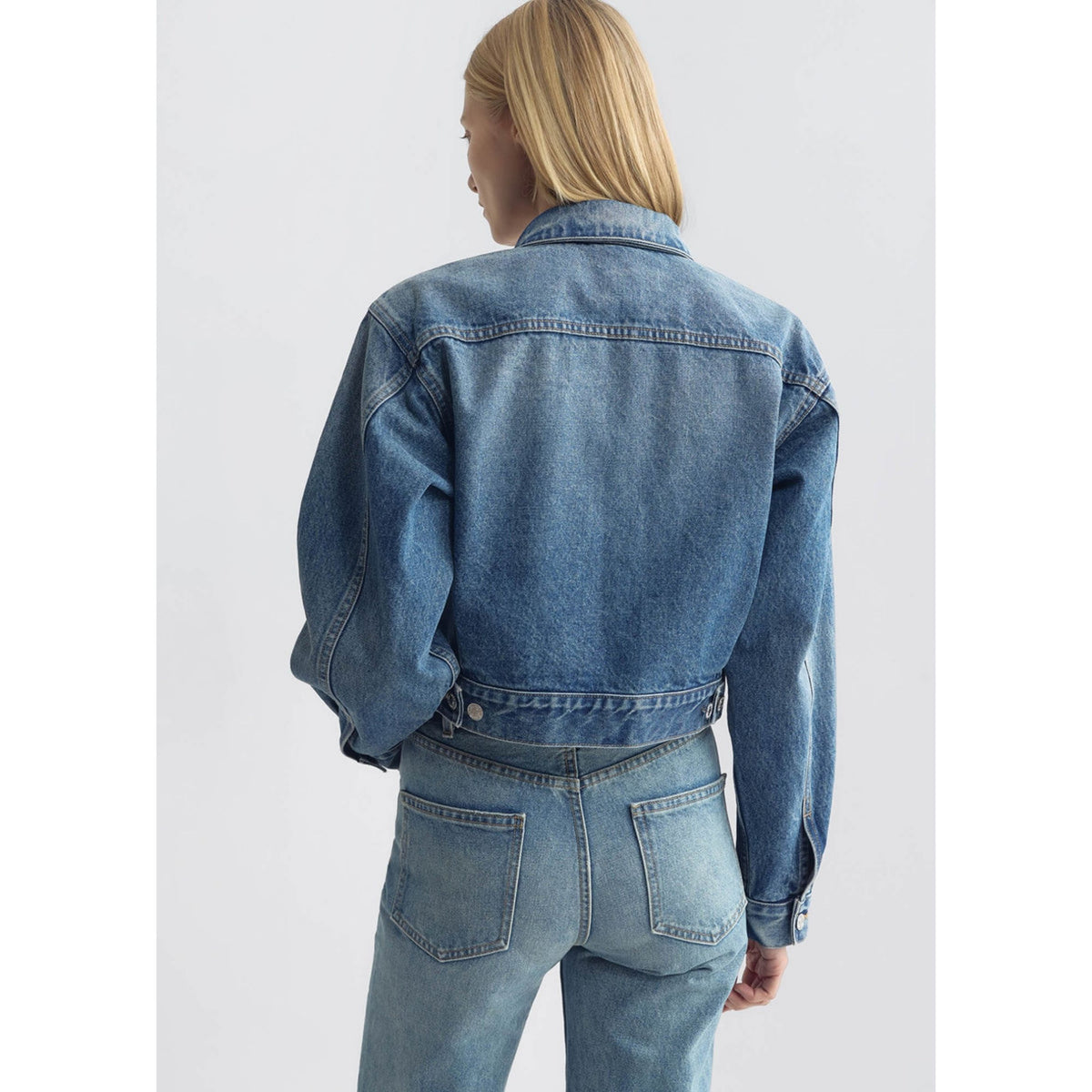Back view of a model wearing the cropped blue denim jacket in Rosebowl Wash with matching jeans.