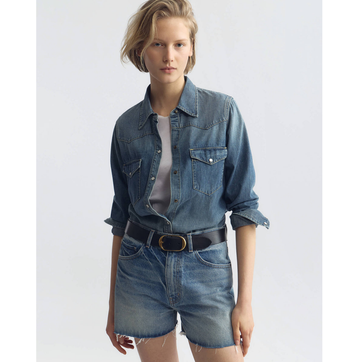 Person wearing a denim shirt and shorts on a white background