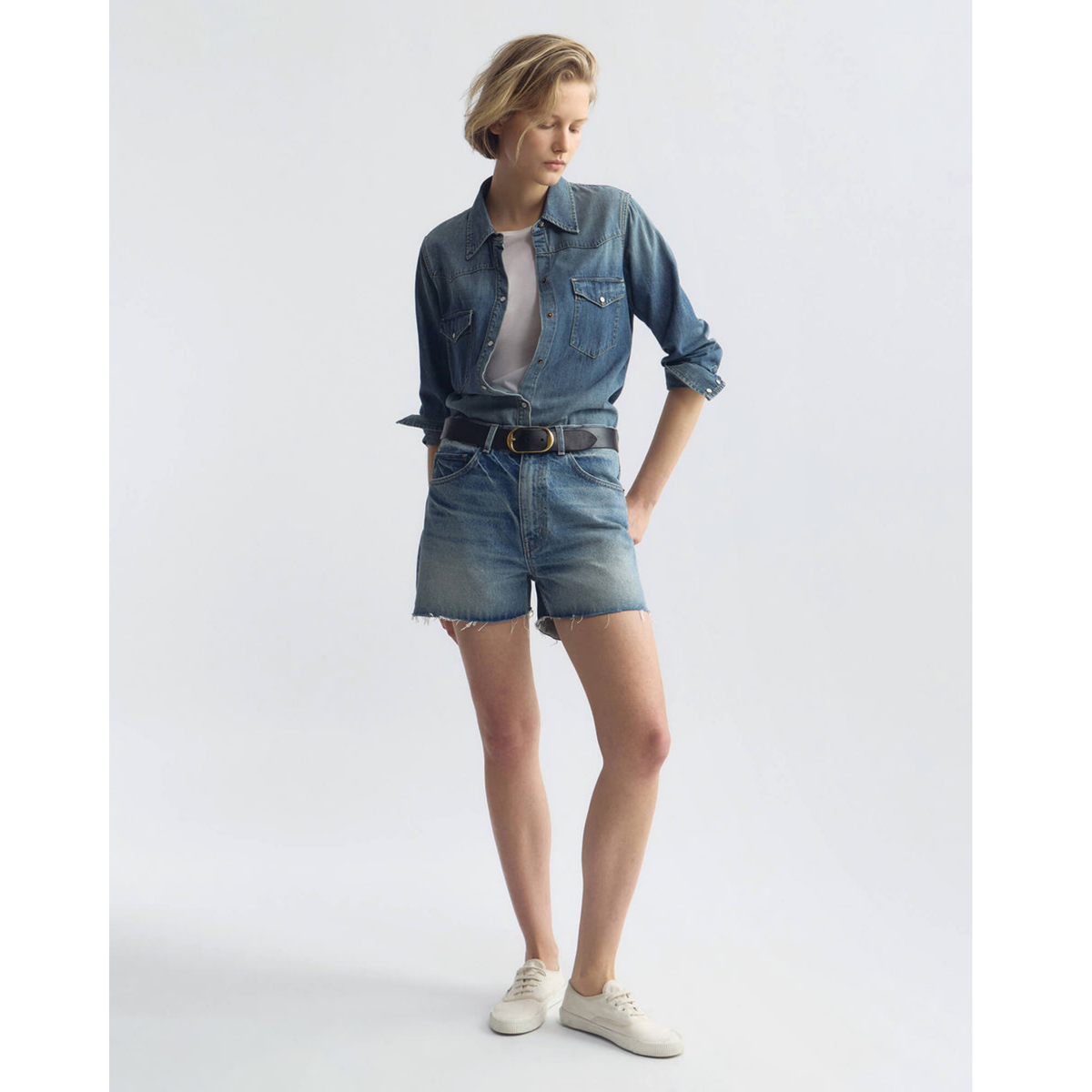 Person wearing a denim outfit with shorts and shirt on a white background
