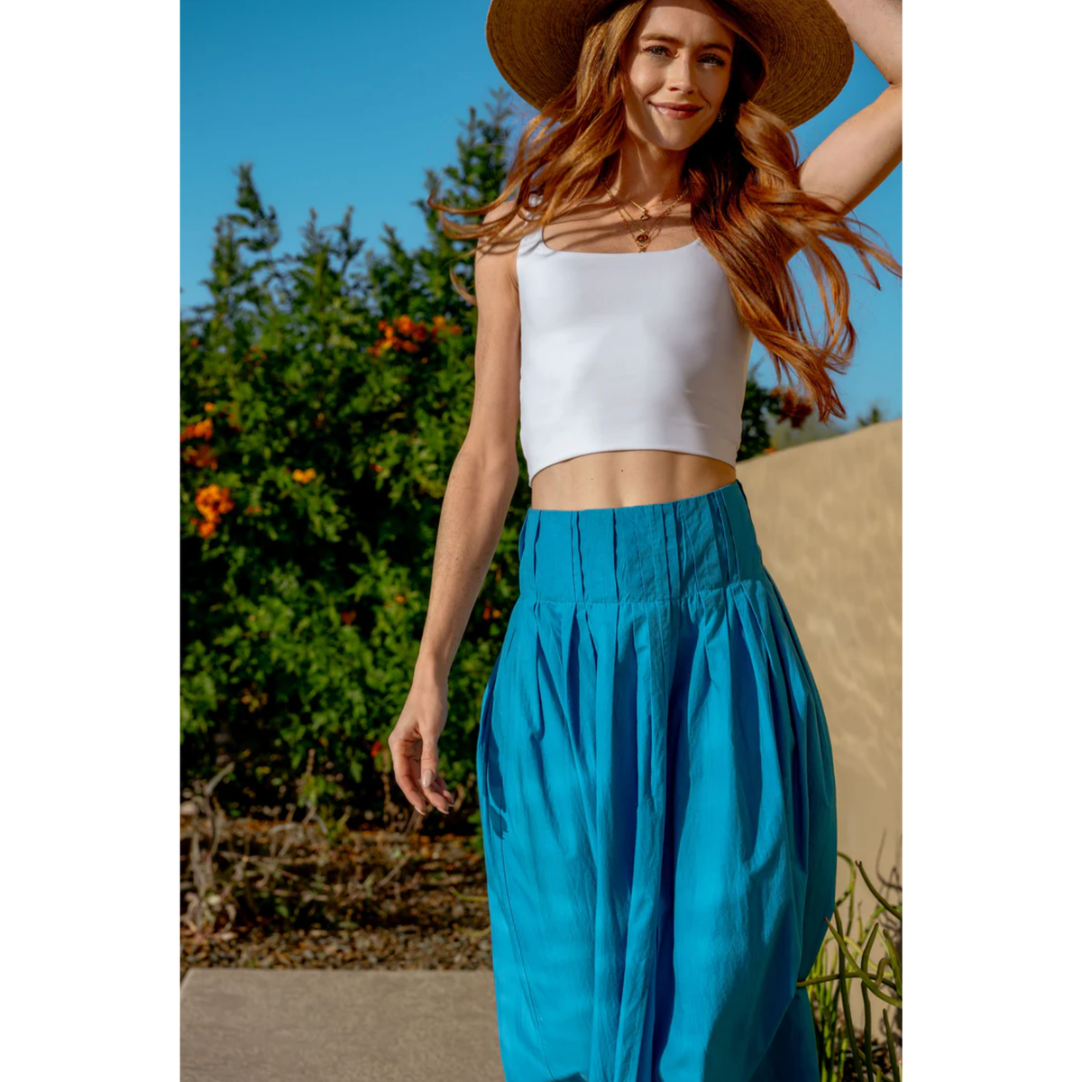 Woman wearing a white top and blue pants with a straw hat outdoors.