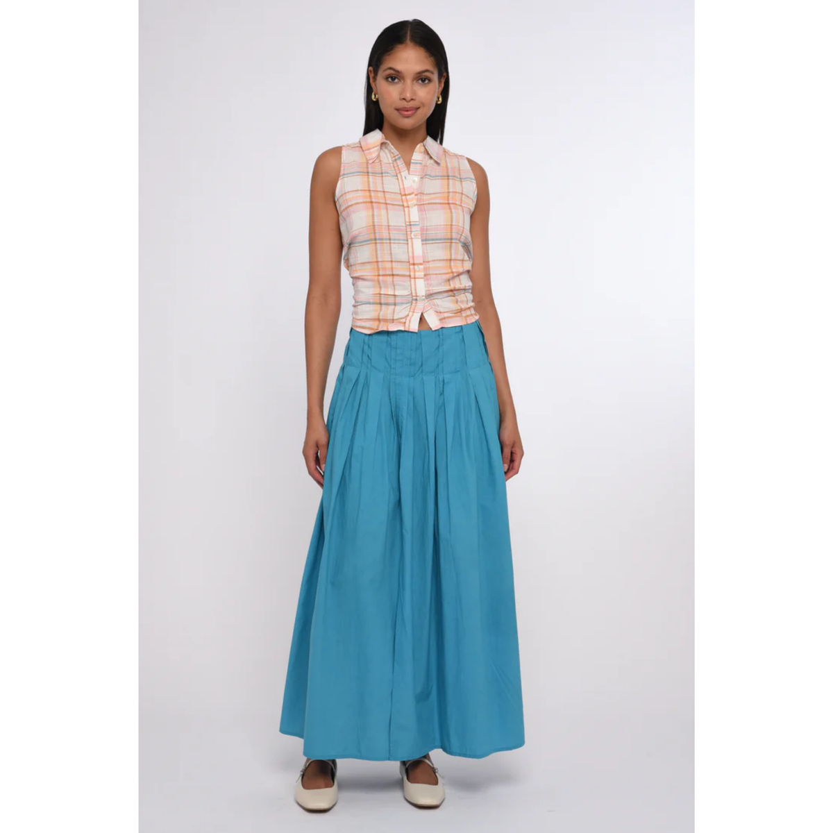 Woman wearing a sleeveless plaid top and blue skirt on a white background