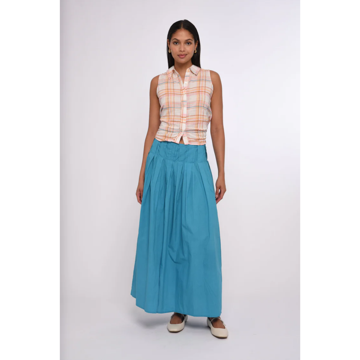 Woman wearing a sleeveless plaid top and blue skirt on a white background