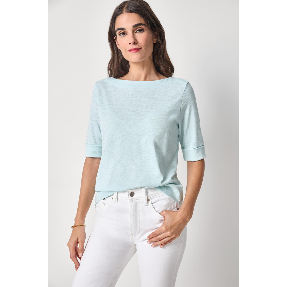 Woman wearing a light blue top and white pants on a plain background