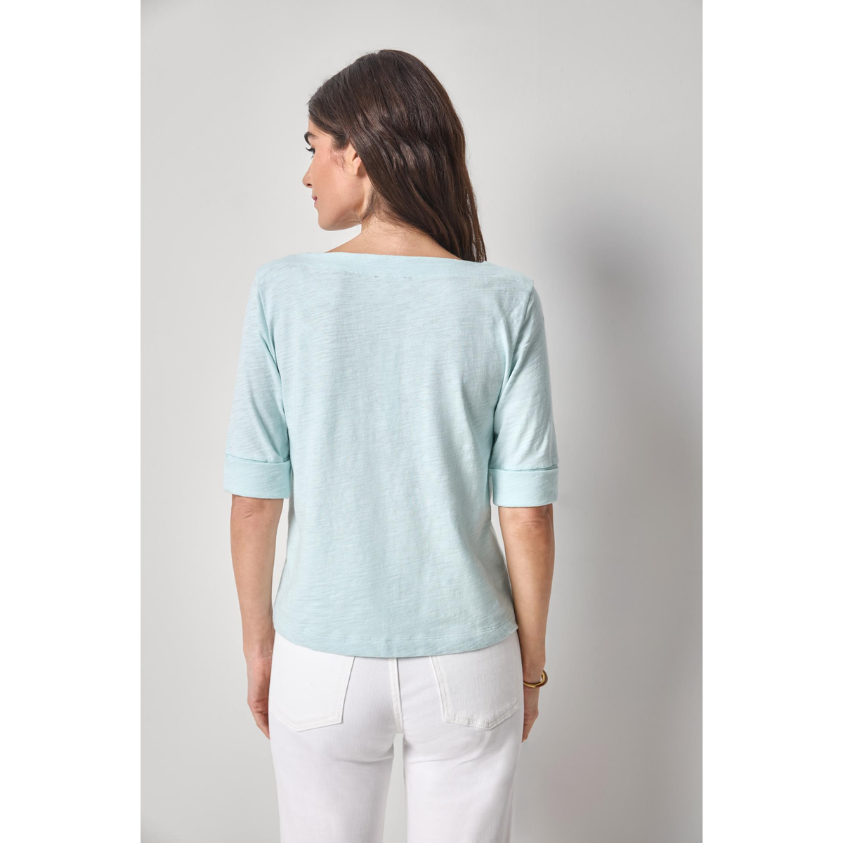 Woman wearing a light blue top and white pants against a plain background