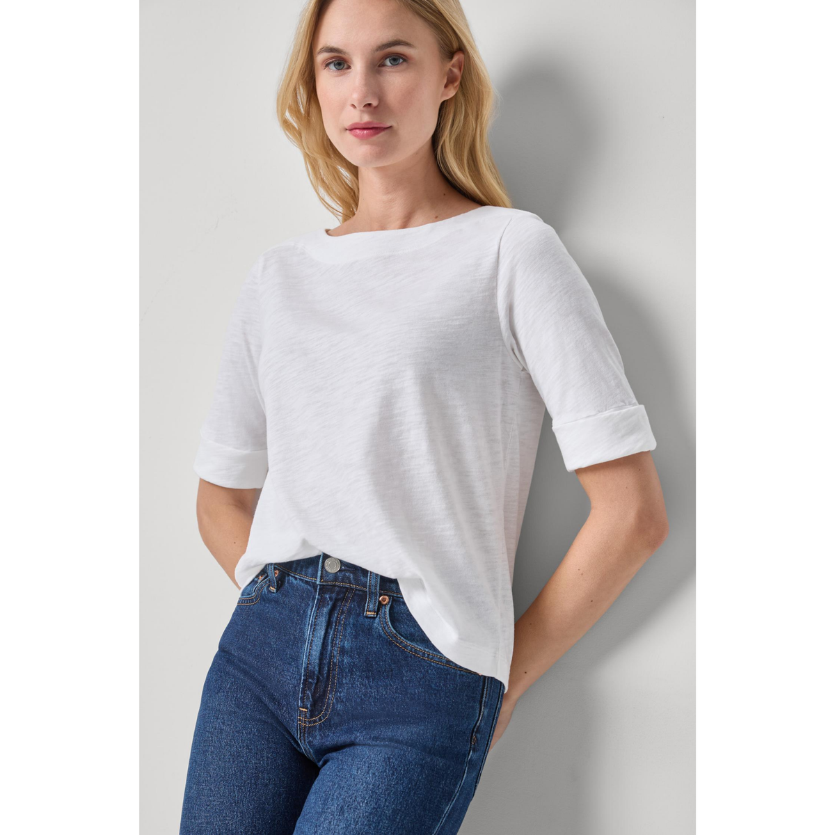 Woman wearing a white t-shirt and blue jeans against a plain background