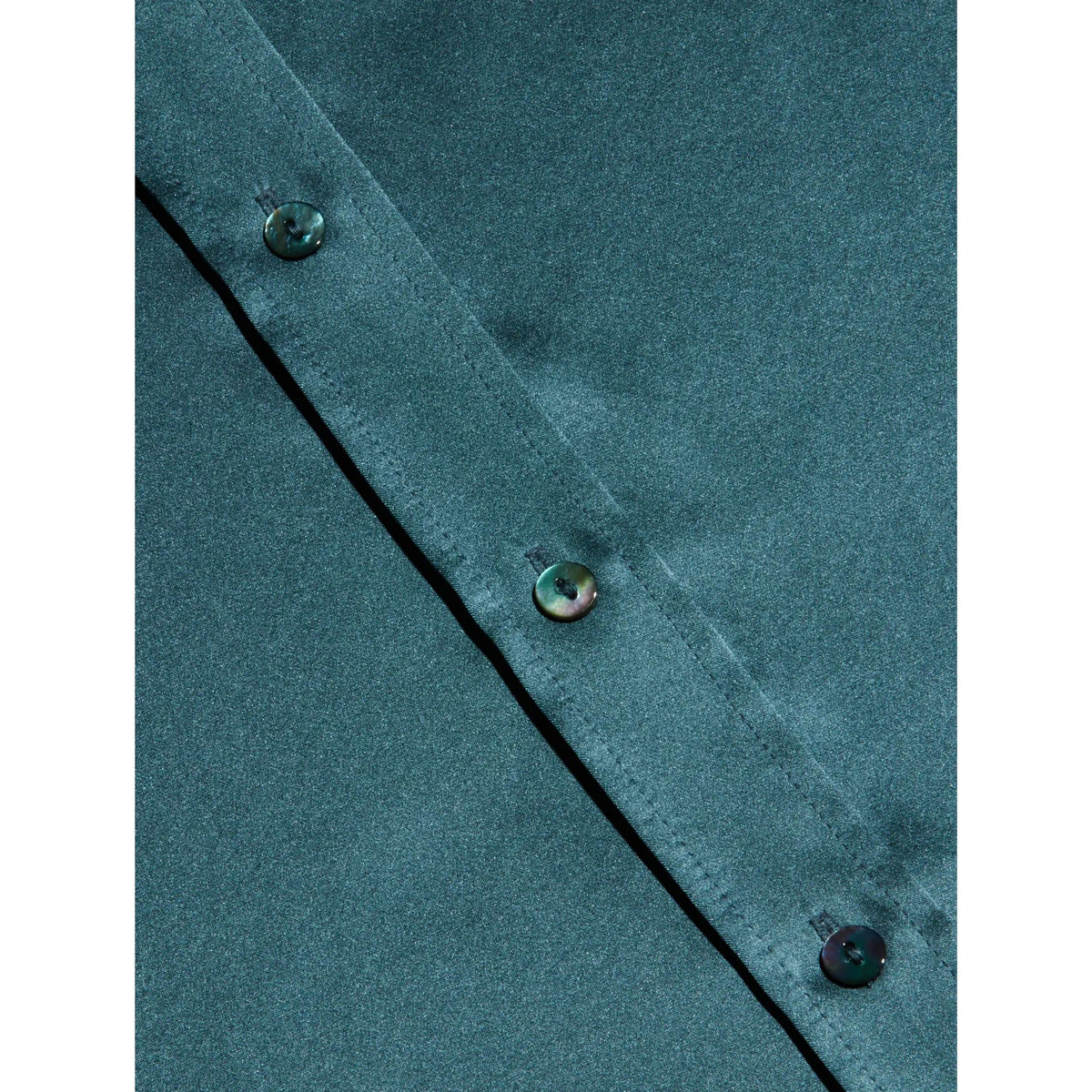 Close-up of a dark teal-green button-down shirt showing the collar, button closure, and diagonal seam detail.