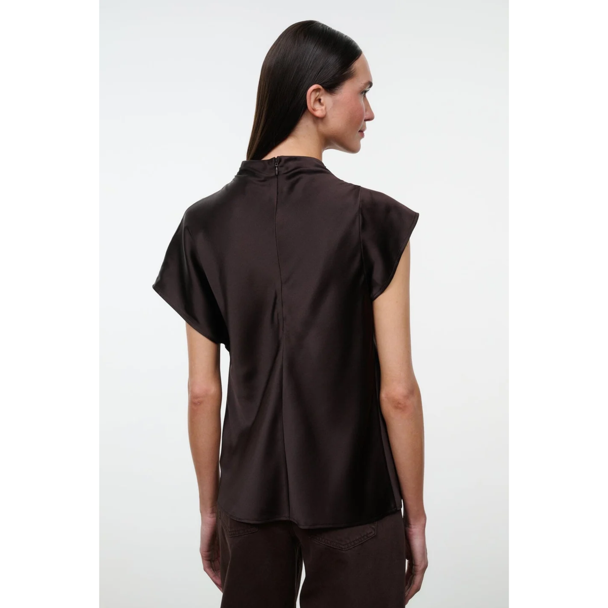 A woman shown from the back wearing a dark brown short-sleeve top with a high gathered neckline and a slight satin sheen, paired with matching dark brown pants, against a light gray studio background.