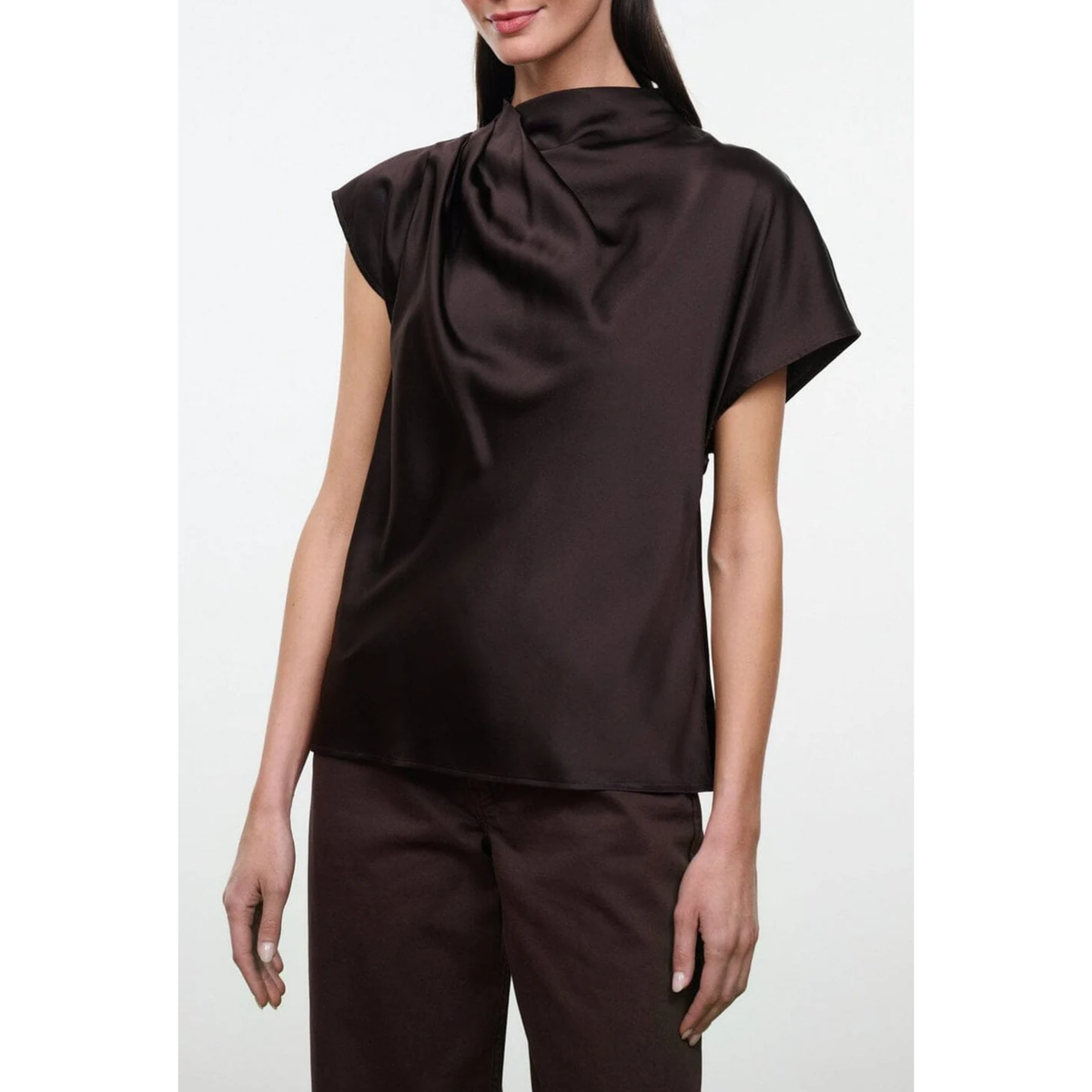 A woman wearing a dark brown draped satin short-sleeve top and matching brown trousers, shown from the lips down against a light gray studio background.