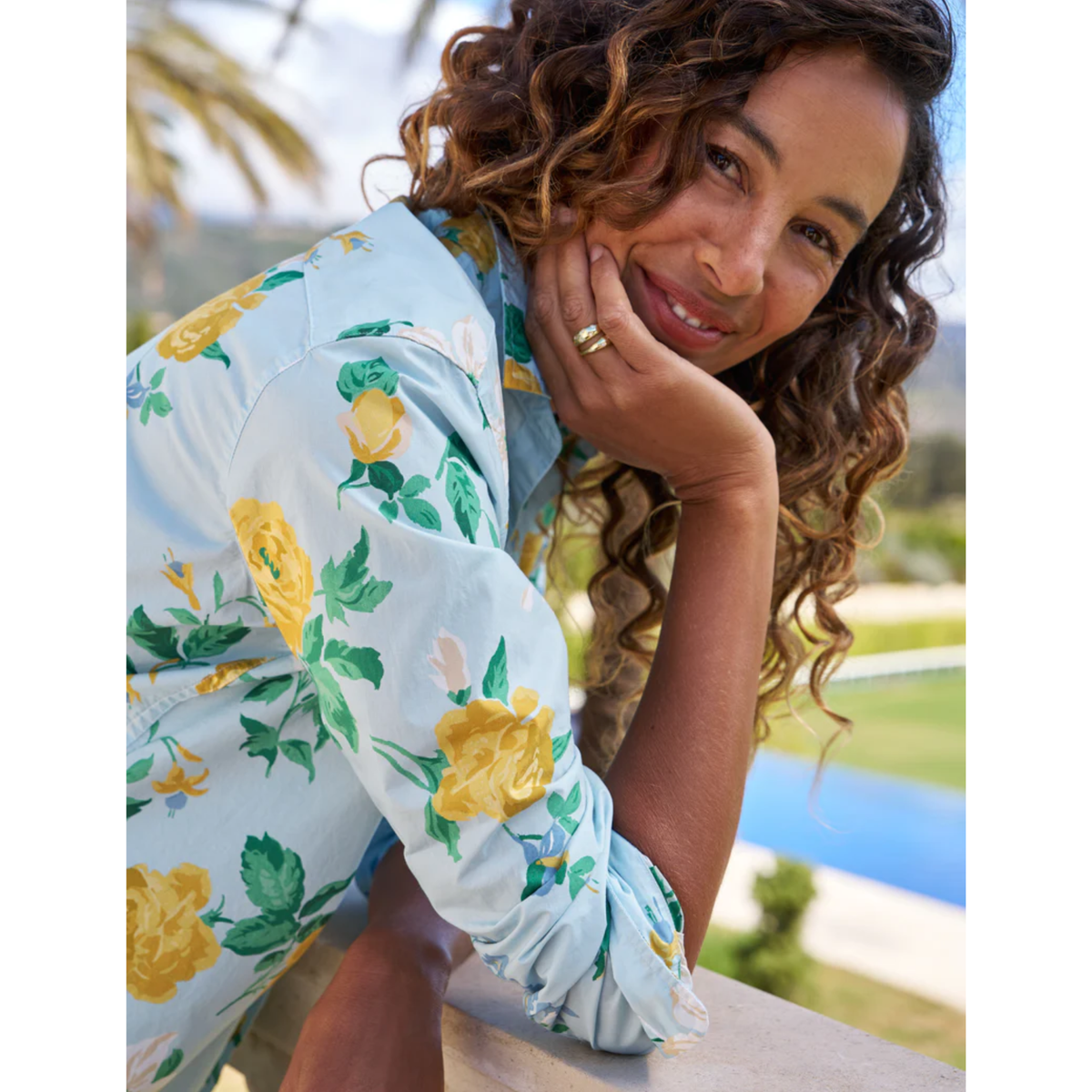 Woman wearing a floral dress with a pool and palm trees in the background