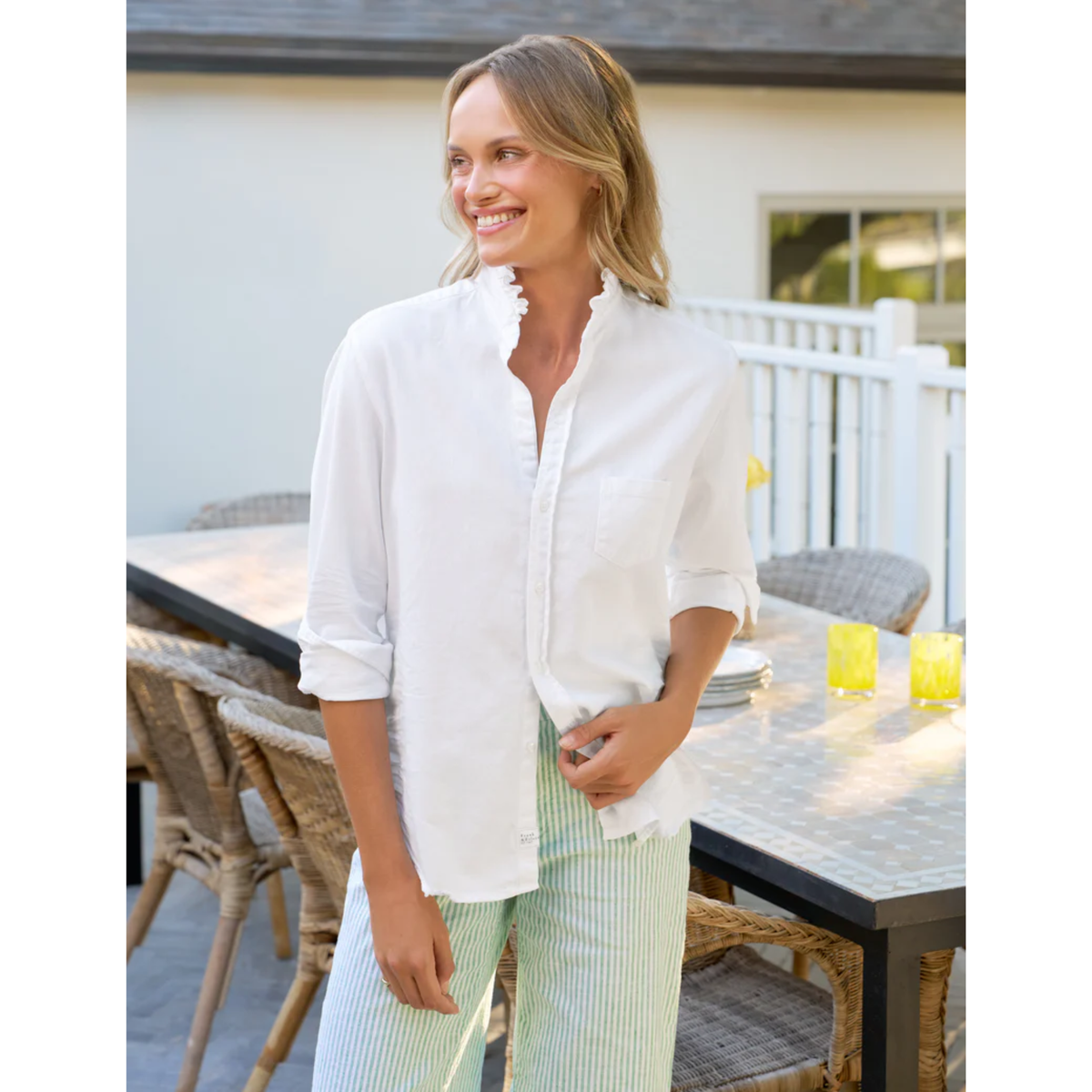 Woman in a white shirt and green pants standing outdoors near a table with candles.
