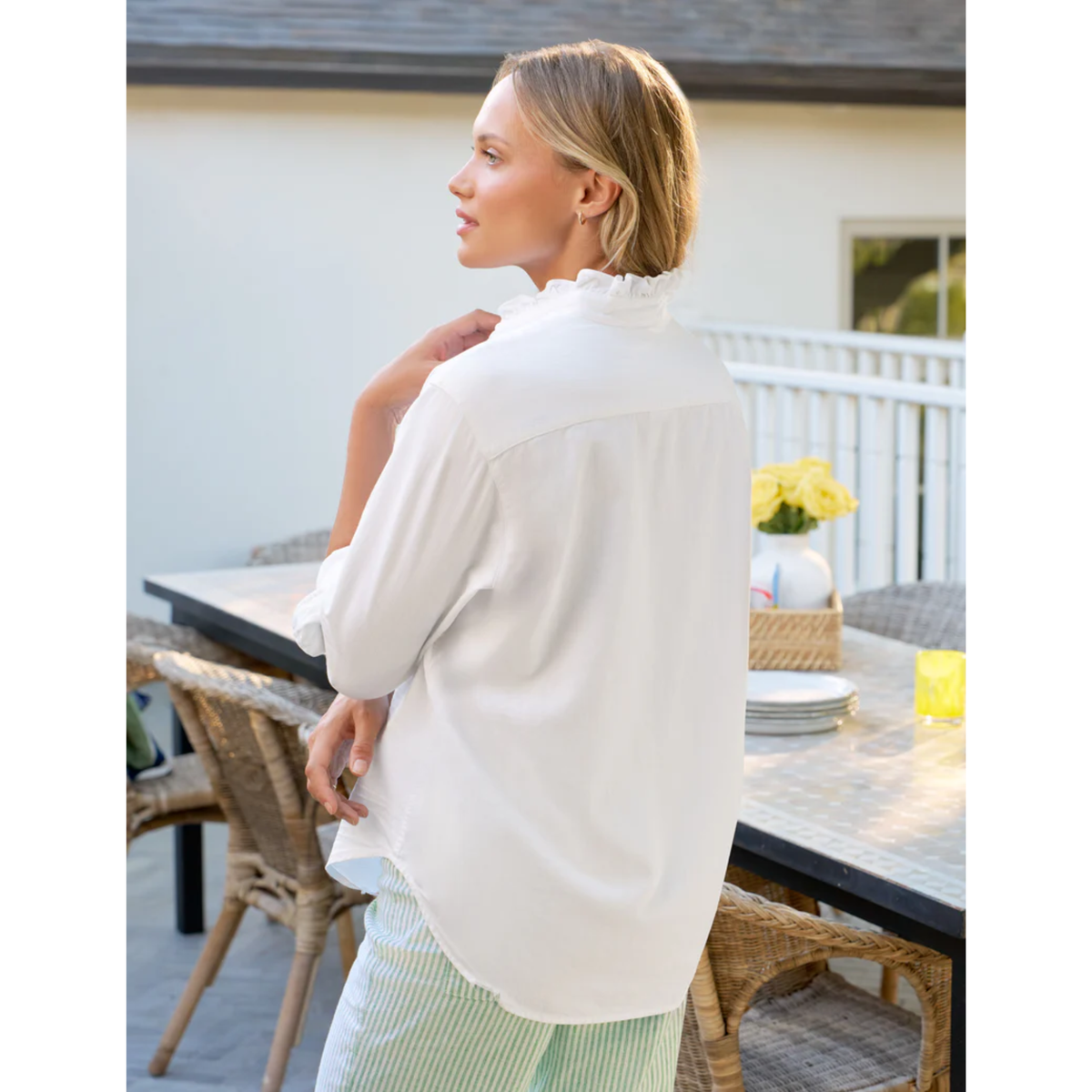 Woman in a white shirt sitting at an outdoor table with a house in the background
