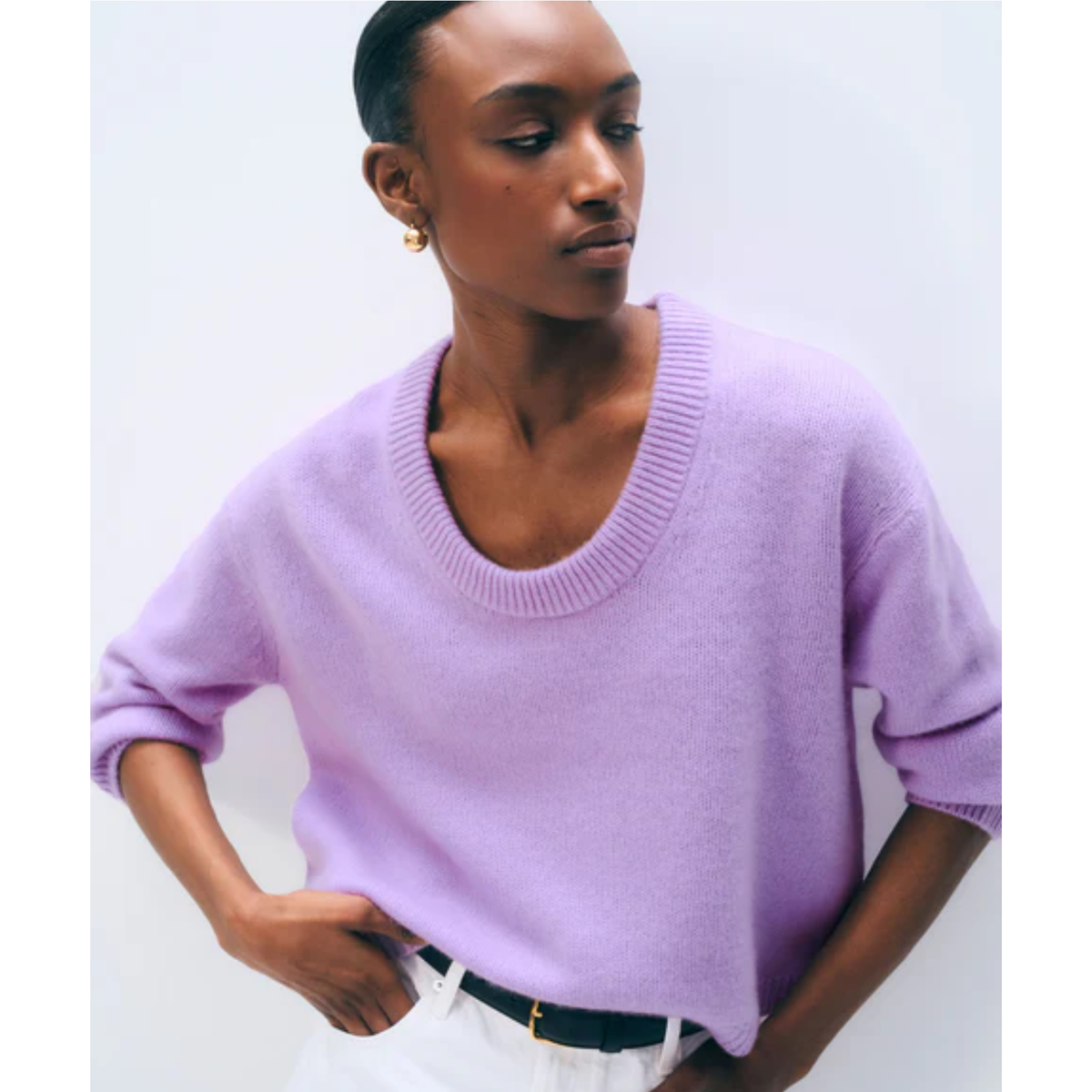 A model wearing a light purple knit crewneck sweater with three-quarter sleeves, paired with white trousers and a black belt, against a plain light gray background.